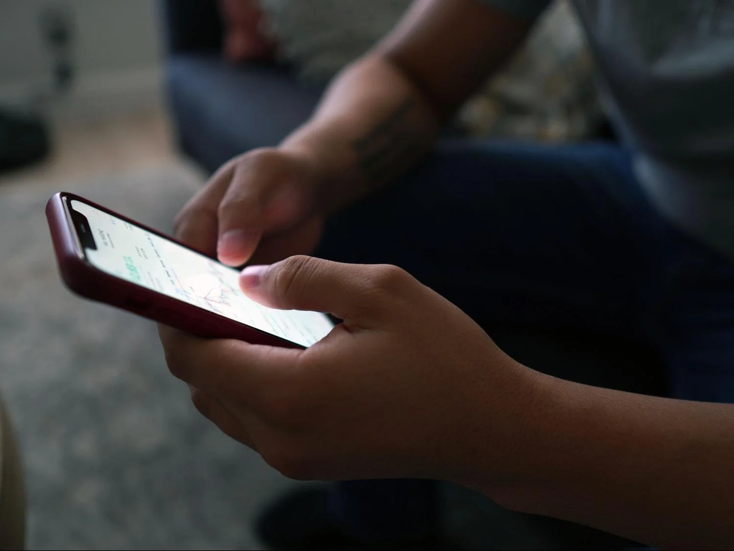 Man's hands holding and scrolling a smartphone while seated indoors, related to anxious attachment patterns in dating.