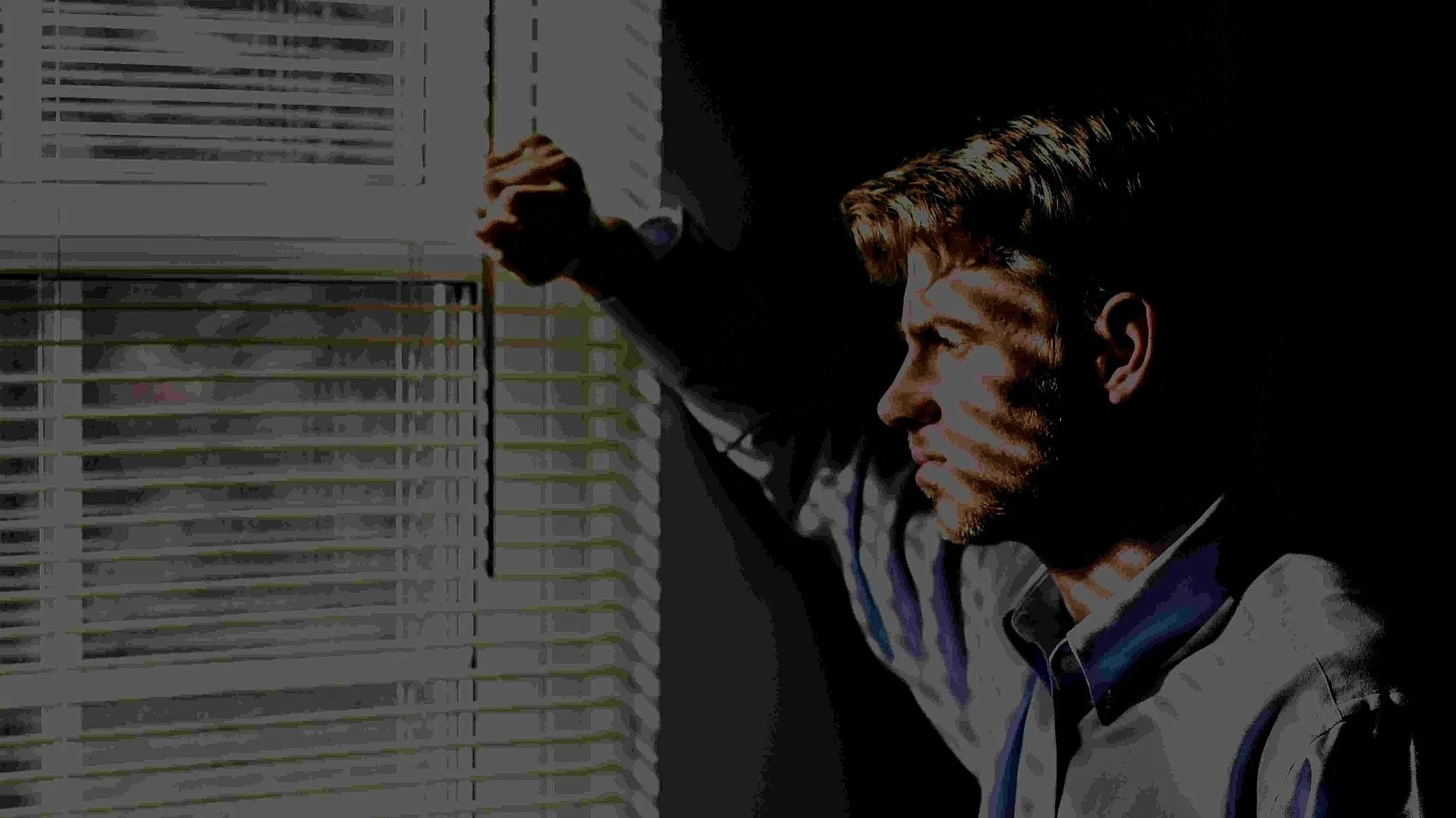 Stylized photo of a man in a shirt and tie looking out through window blinds, representing the anxiety and hypervigilance addressed in individual therapy for men in Mooresville, NC.