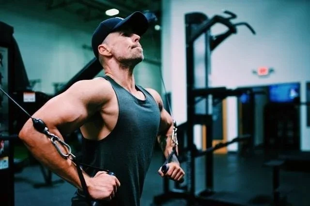 Man using a cable machine at the gym, representing how men often optimize their bodies and routines while avoiding the root issues therapy is built to address.