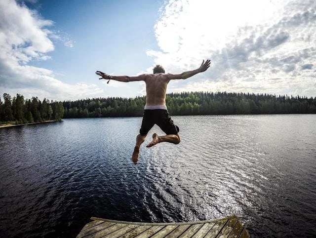 Man leaping off a dock into a lake, arms outstretched, representing the freedom on the other side of confronting the root issue instead of managing it forever.