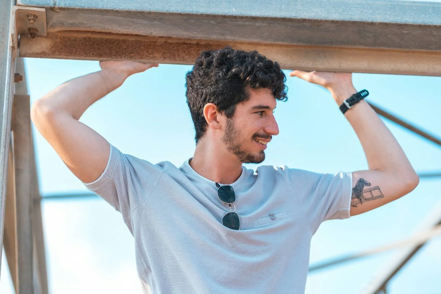 Young man with tattoo smiling outdoors, arms raised, representing integrated faith and life in Catholic Christian therapy for men.