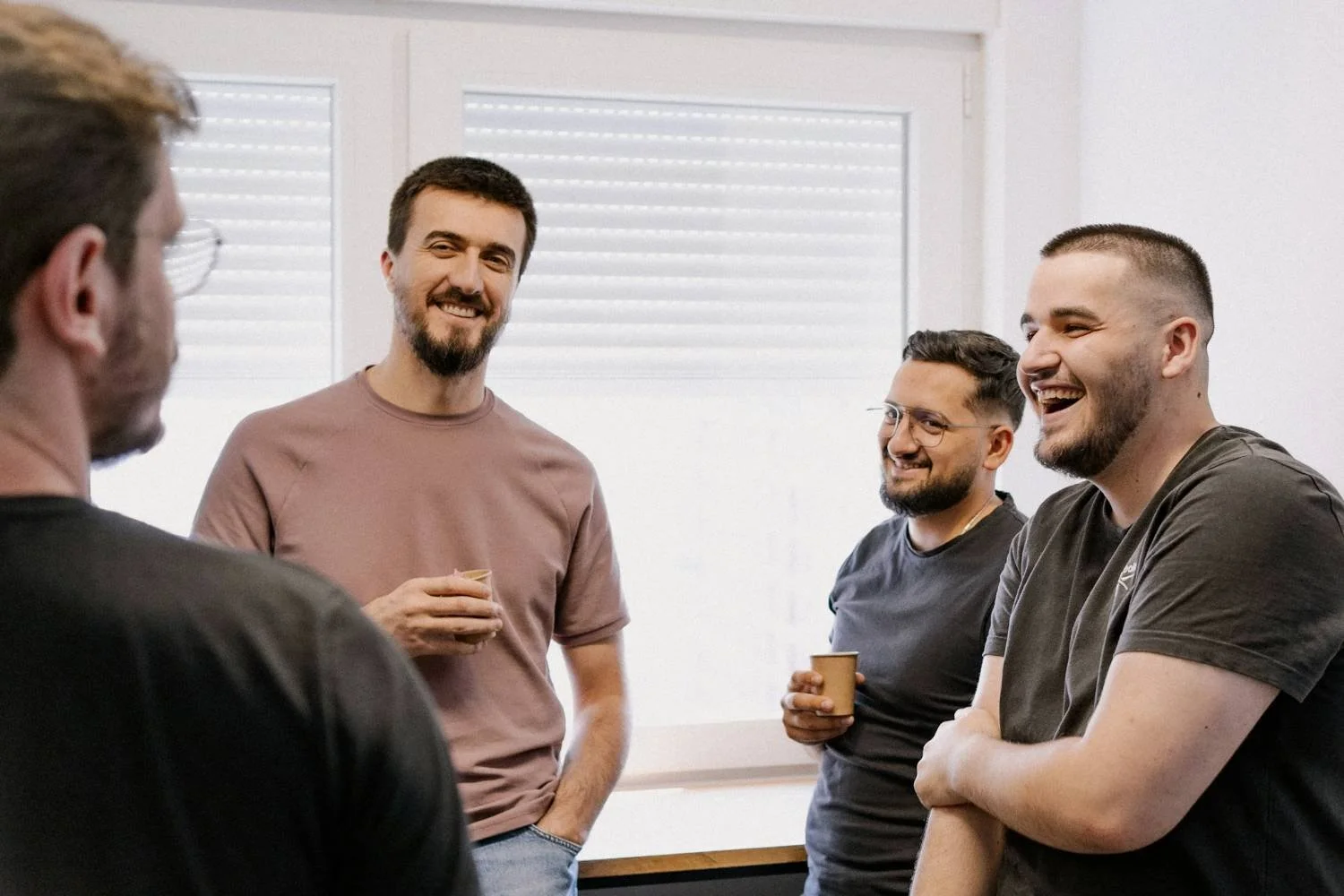 Four men in casual clothing standing indoors holding coffee cups, used for men's anxiety counseling in Mooresville NC.