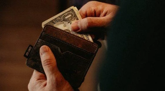 Close-up of a man's hands pulling cash from a worn leather wallet, representing the version of "having it together" that doesn't touch what's actually running the show.