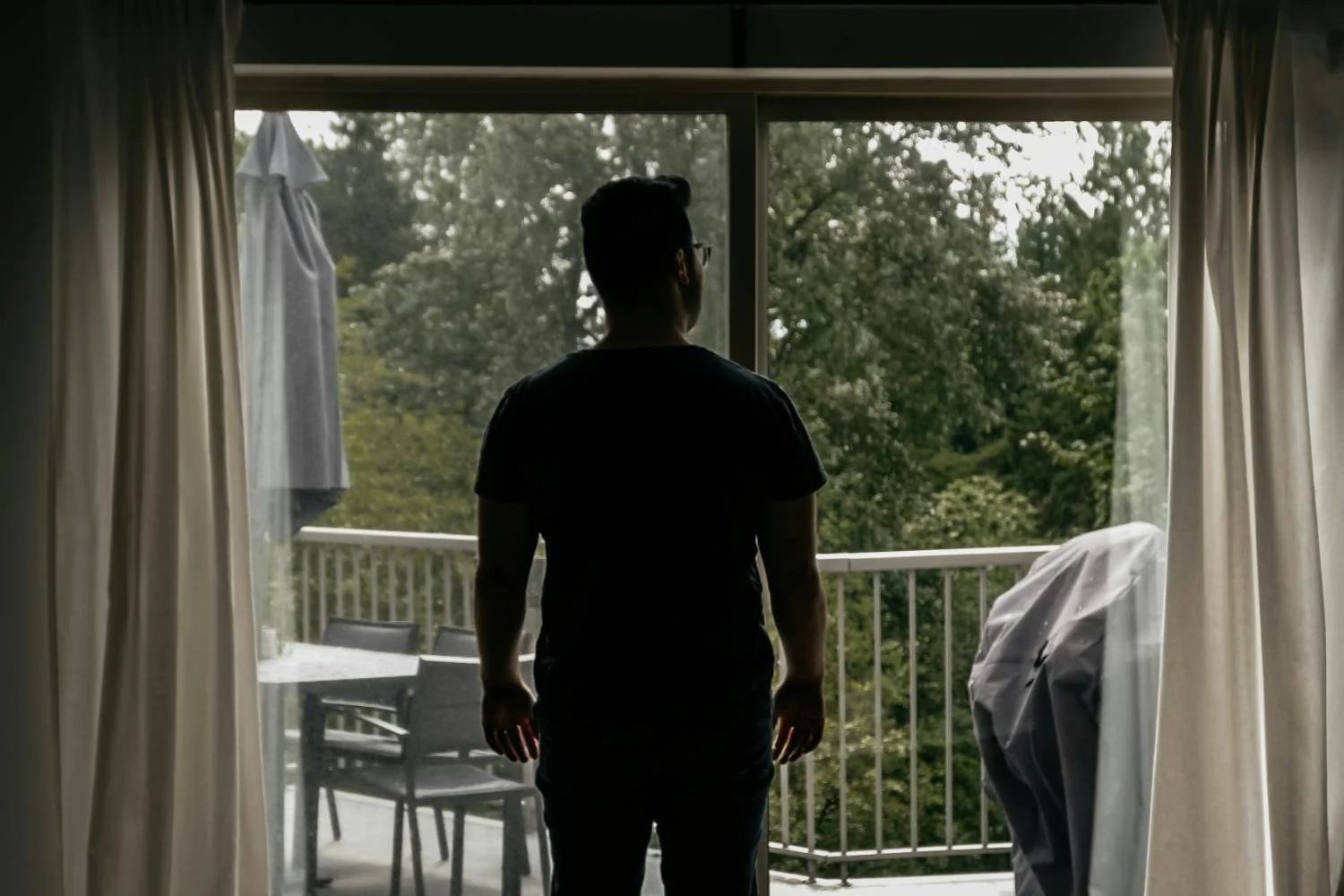 Man seen from behind standing at a sliding glass door, representing relationship cycle distress in therapy for toxic relationships.