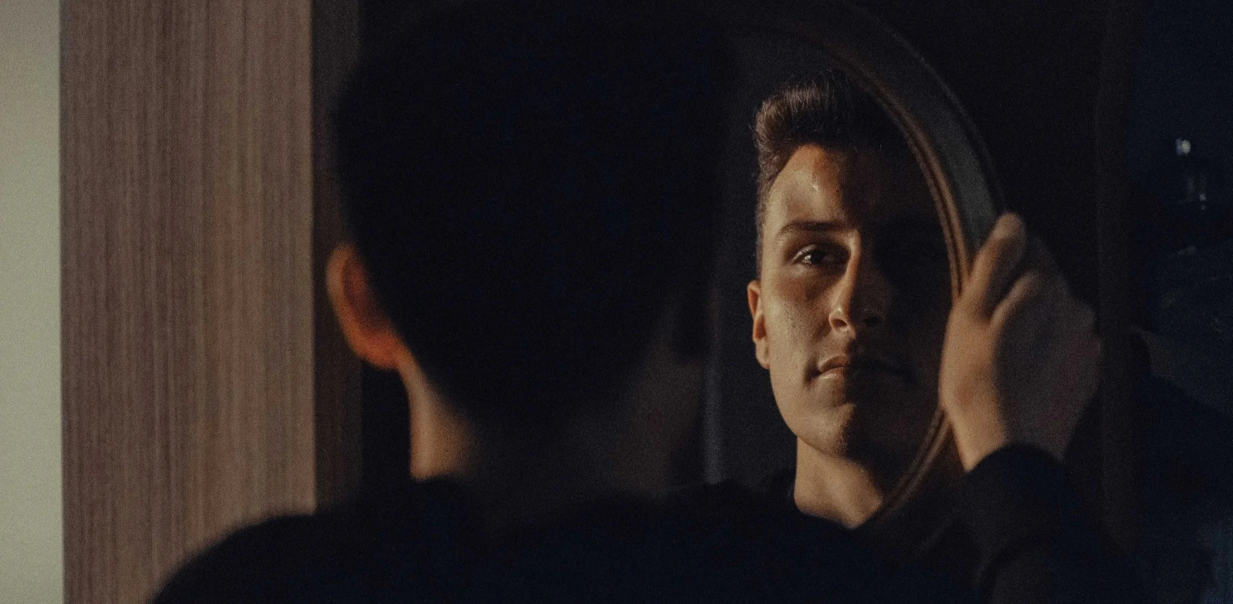 Young man touching a round mirror and looking at his reflection, representing attachment therapy for men in Mooresville, NC.