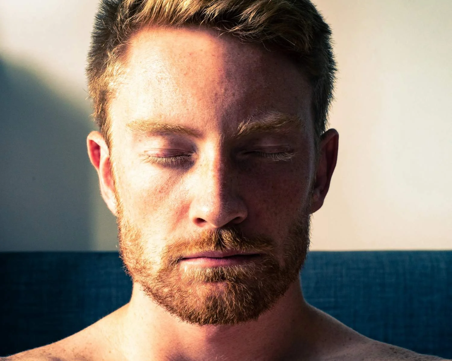 Bearded man with eyes closed and head bowed seated on a couch, representing scrupulosity and religious anxiety treatment in North Carolina
