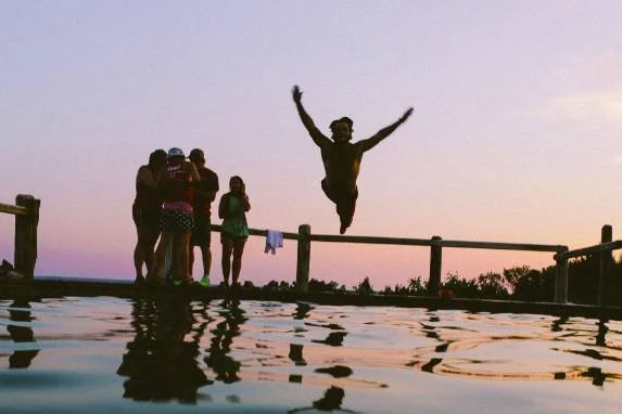 Man leaping from a dock into water at sunset with a group of friends, representing life after scrupulosity and religious OCD treatment.
