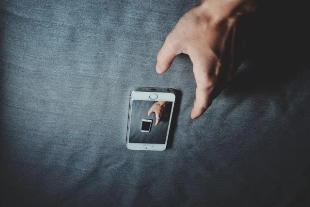 A person taking a selfie with a smartphone, capturing their hand and the device reflecting in the phone's screen