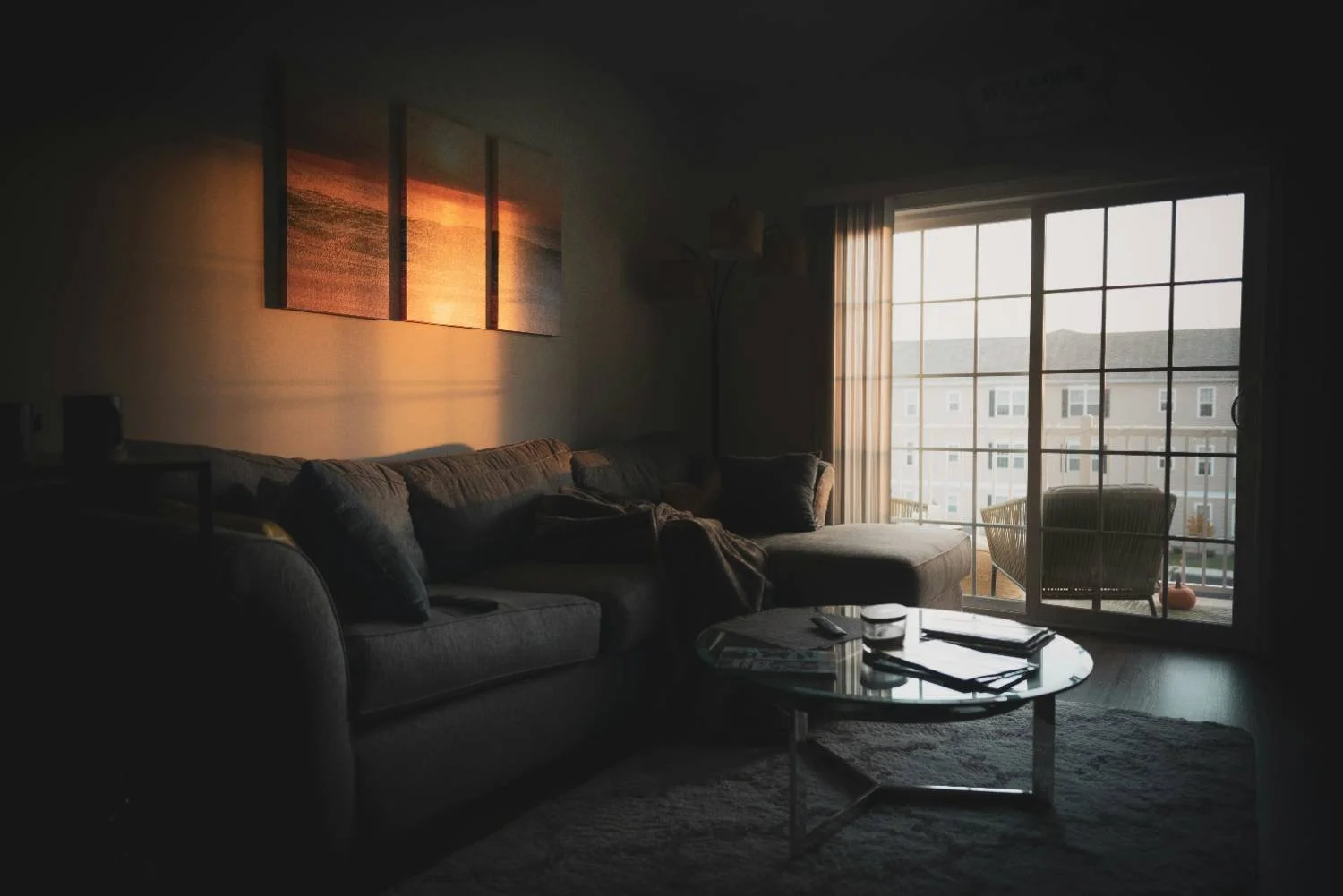 Empty sectional sofa and glass coffee table in a dim living room, representing relationship conflict cycles in men's therapy.