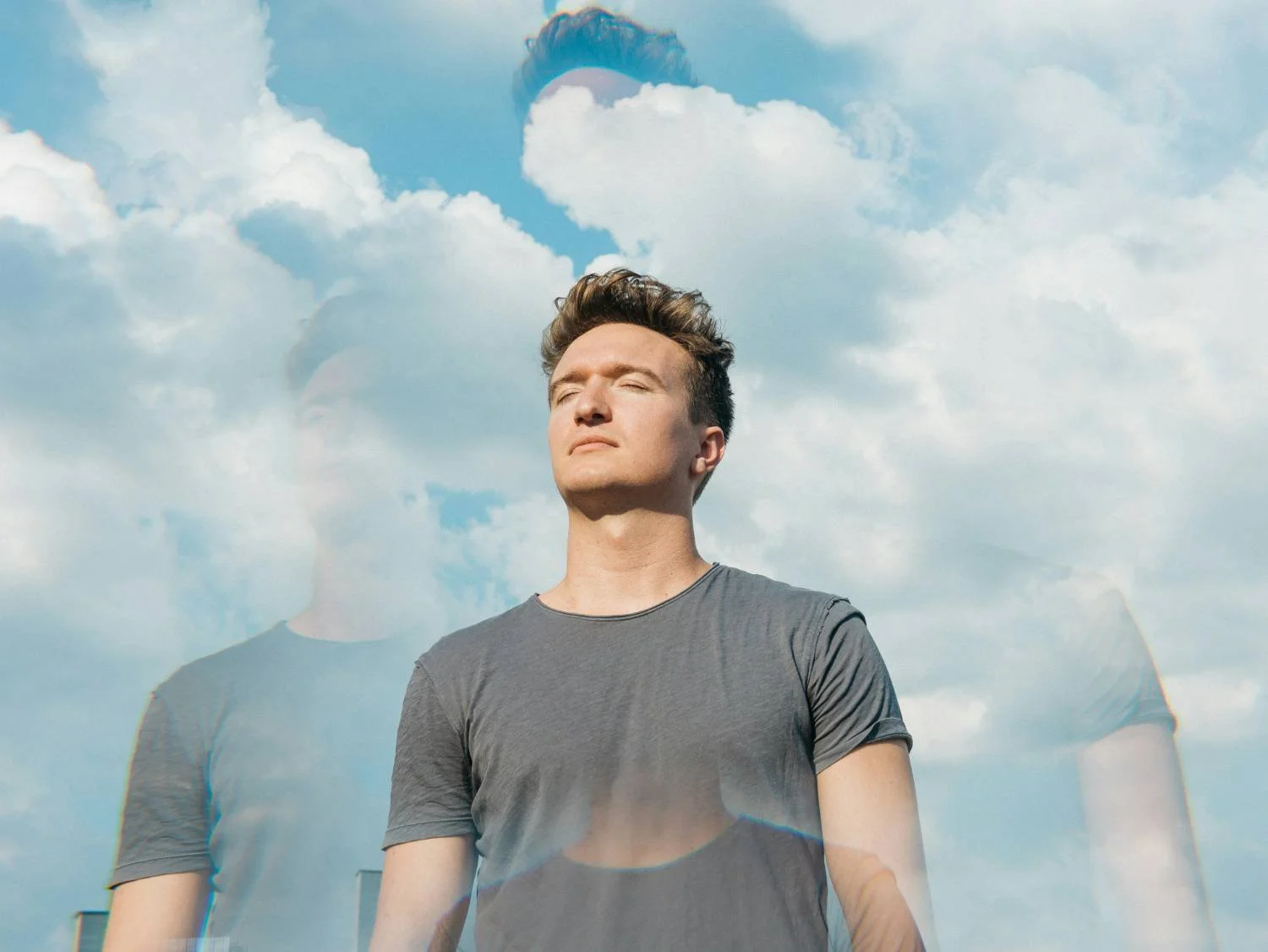 Young man standing outdoors with eyes closed against a cloudy sky, double-exposure effect, ERP treatment for scrupulosity and religious OCD in North Carolina