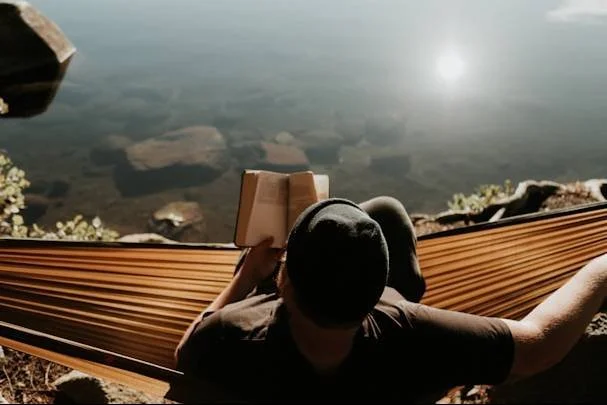 Man lying in hammock reading a book overlooking a lake, representing life after scrupulosity and religious OCD treatment in Mooresville, NC.