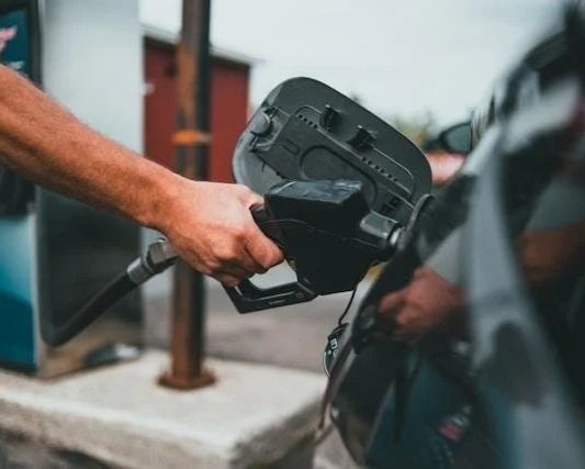 Close-up of a man's hand at a gas pump, representing the routines that hold together on the surface while the same pattern keeps repeating underneath.