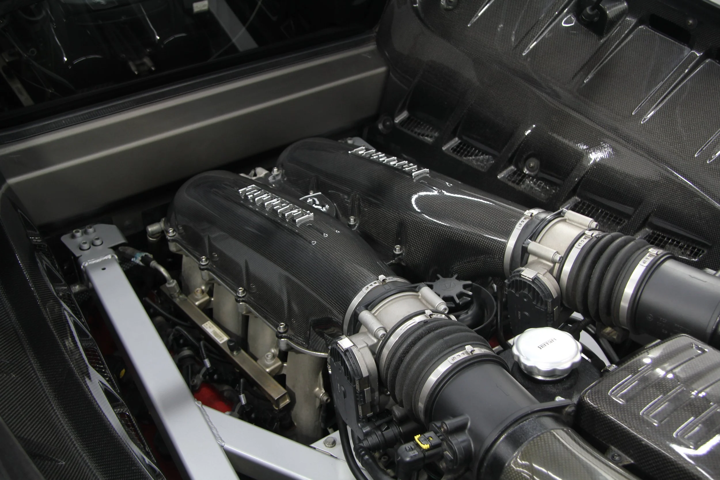 Close-up of a Ferrari engine with carbon fiber covers and intake manifold.