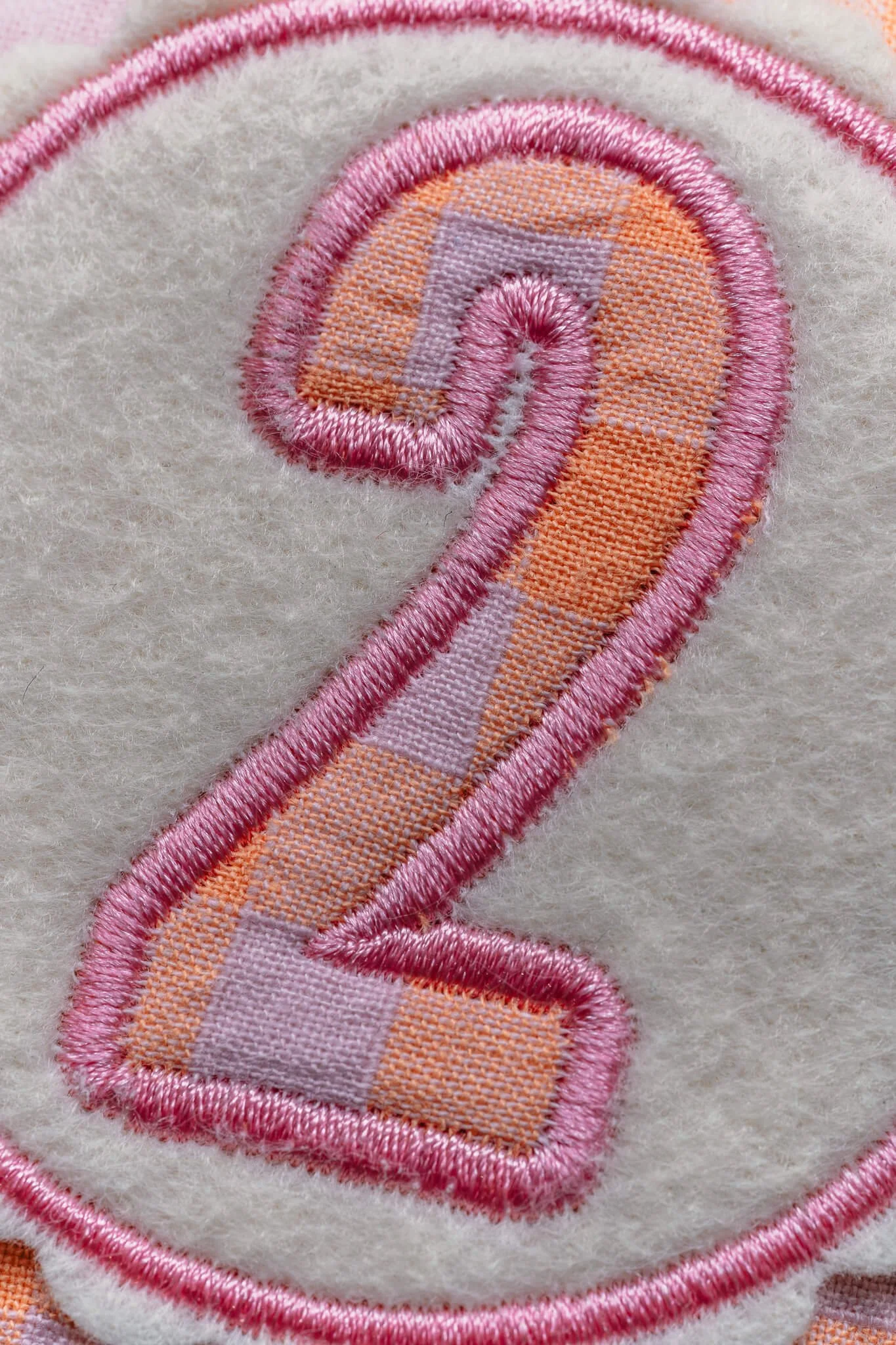 Close-up of an embroidered design featuring a pink and orange rainbow with a fluffy white background.