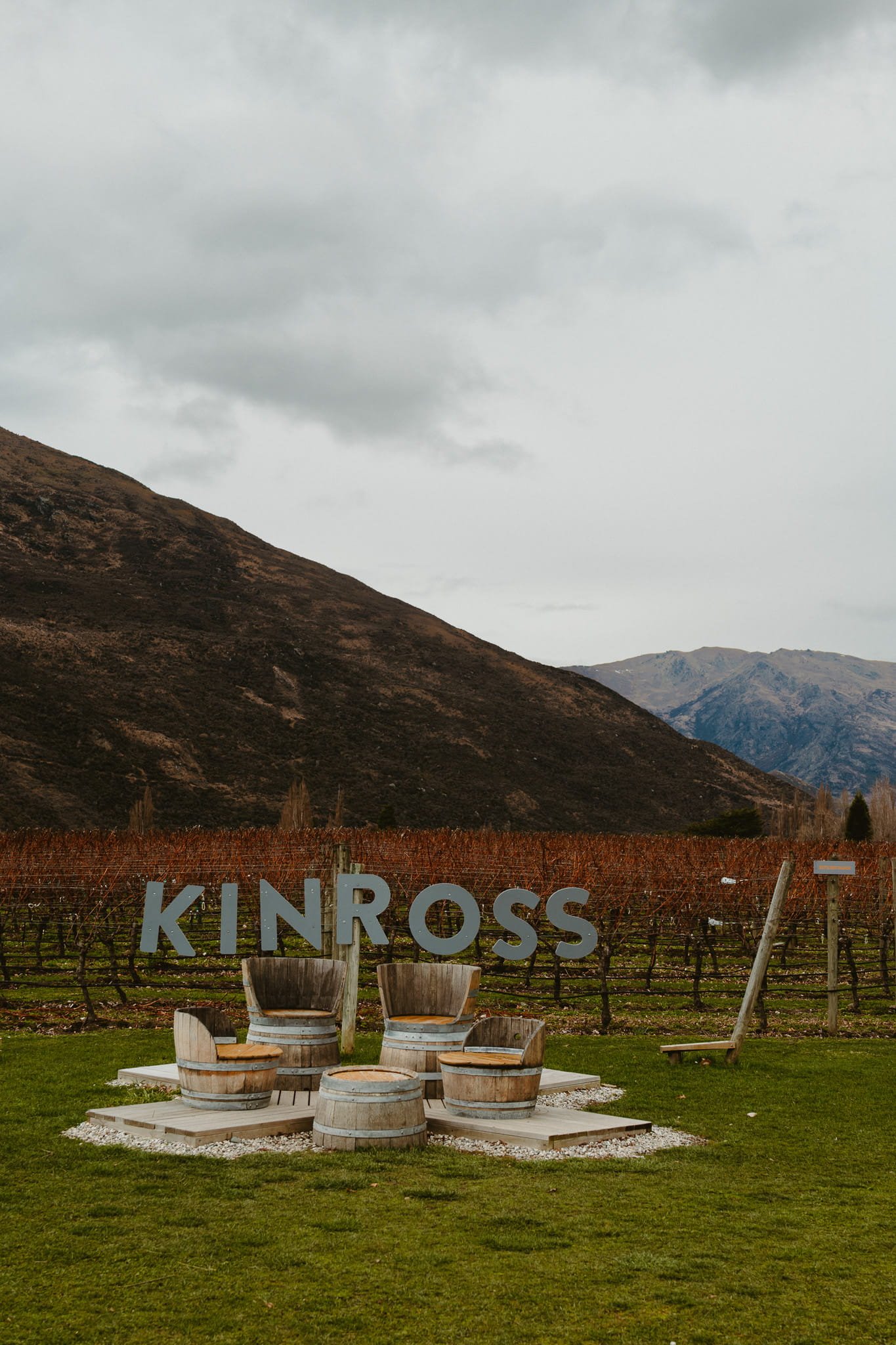 Kinross winery sign in front of winter vineyard rows with mountains behind, Gibbston Valley