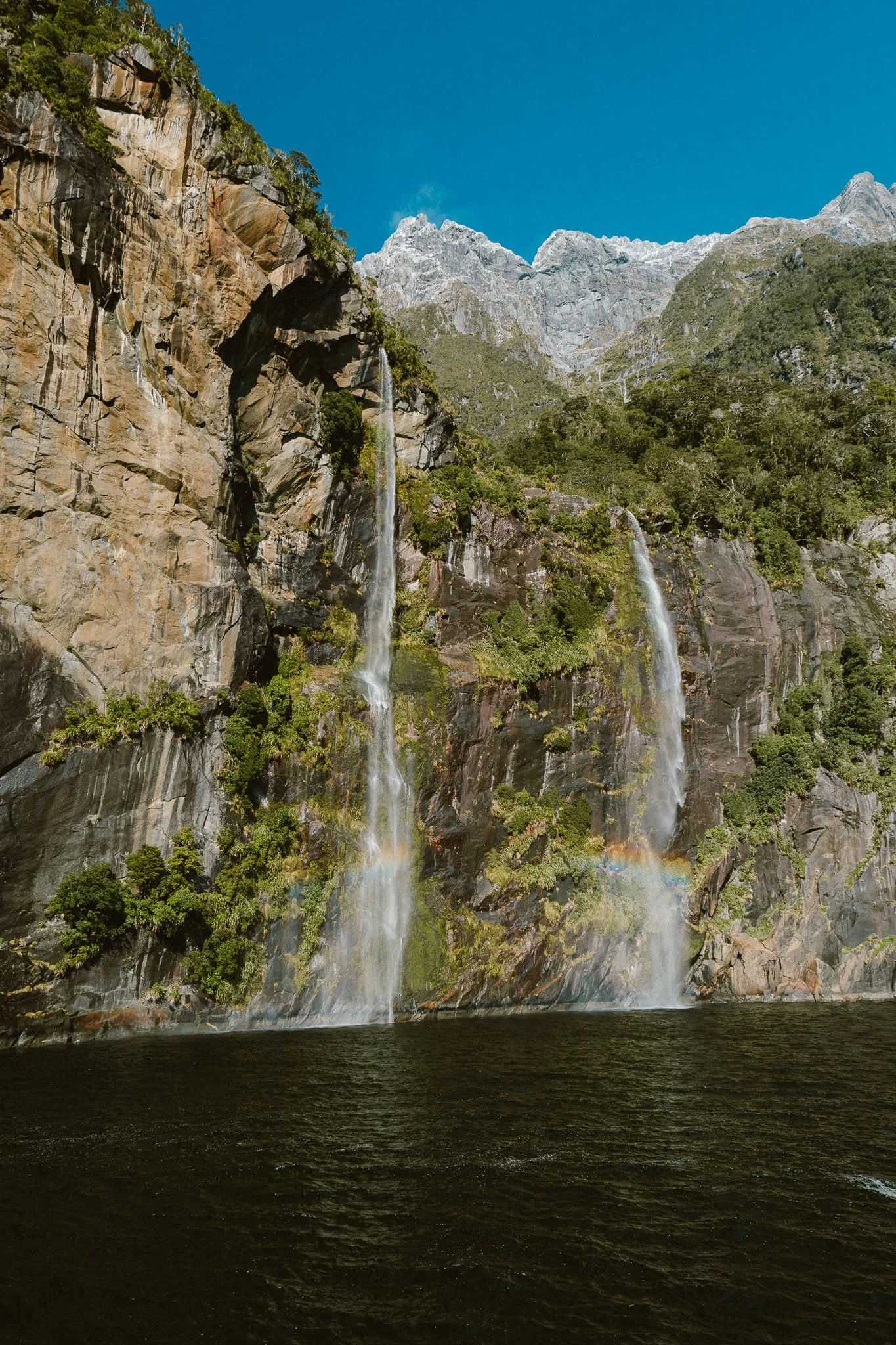 Waterfall cascading down sheer rock face into Milford Sound fiord
