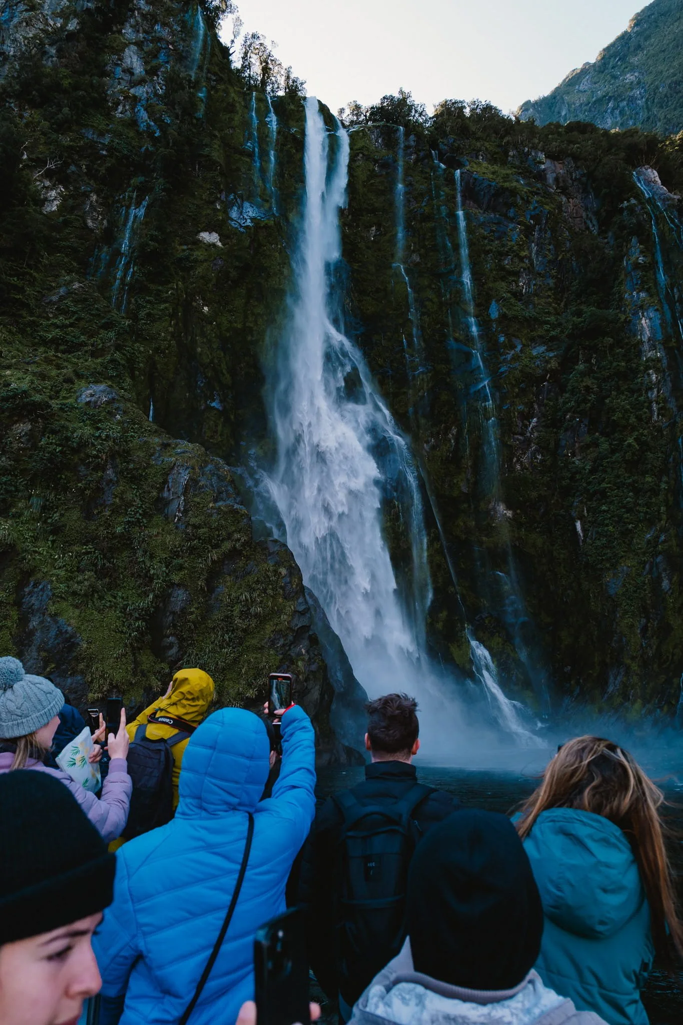 Tourists photographing a large waterfall from a cruise boat at Milford Sound