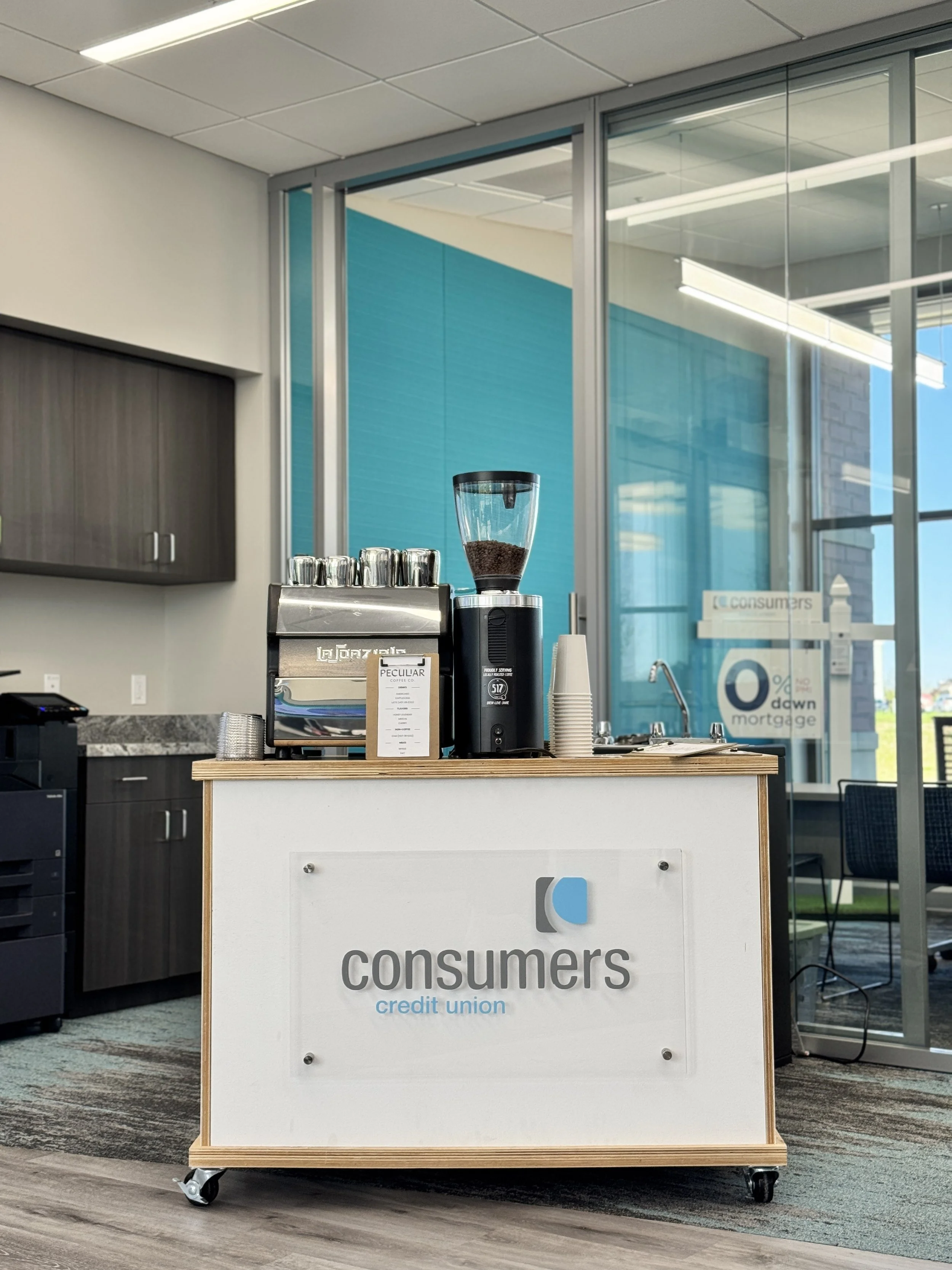 A mobile coffee cart in an office, with a custom sign that says "Consumers Credit Union."