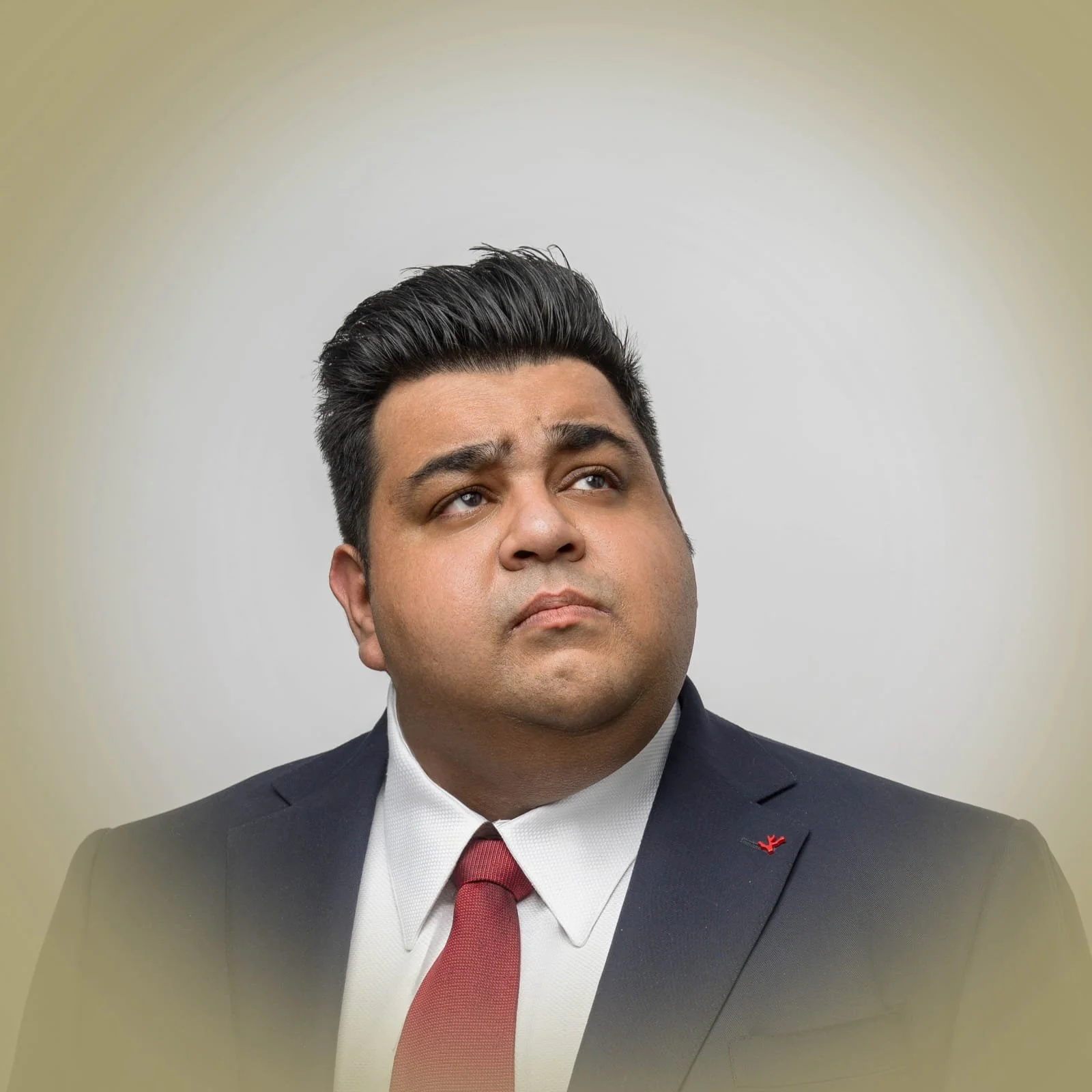 A man in a suit with a red tie and white shirt, looking upward with a serious expression, against a plain background with a yellowish hue.