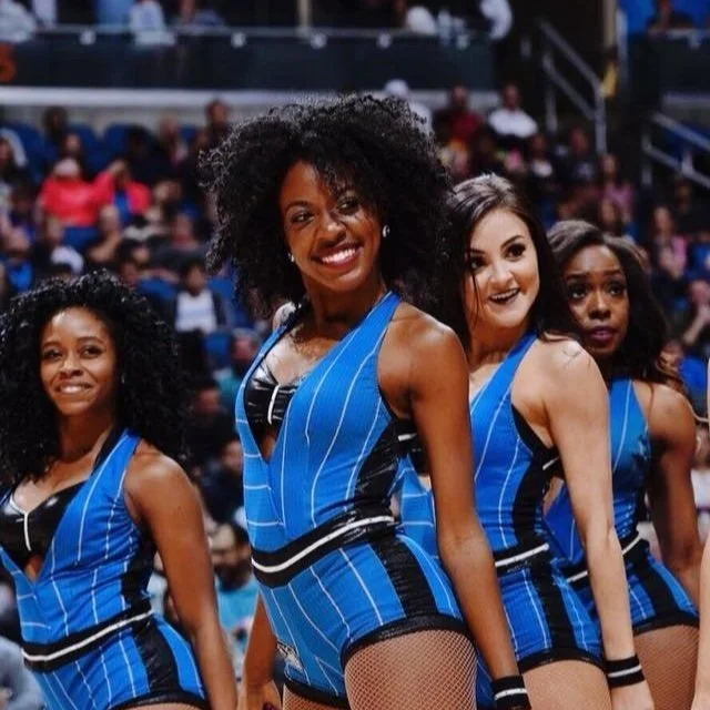 A group of four cheerleaders smiling and posing in blue and black uniforms during a sports event.