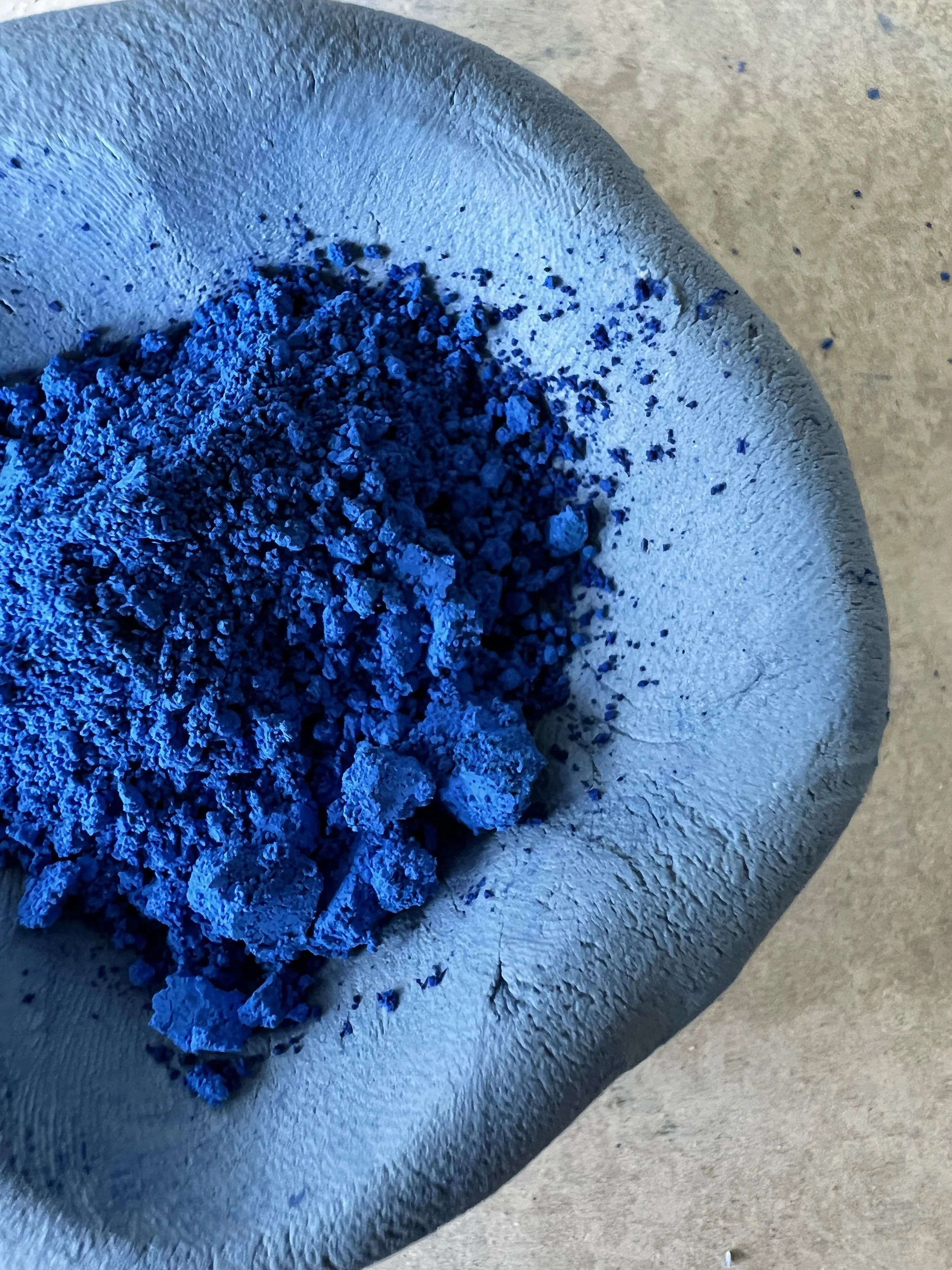 Close-up of blue powder or pigment in a textured ceramic bowl on a beige surface.