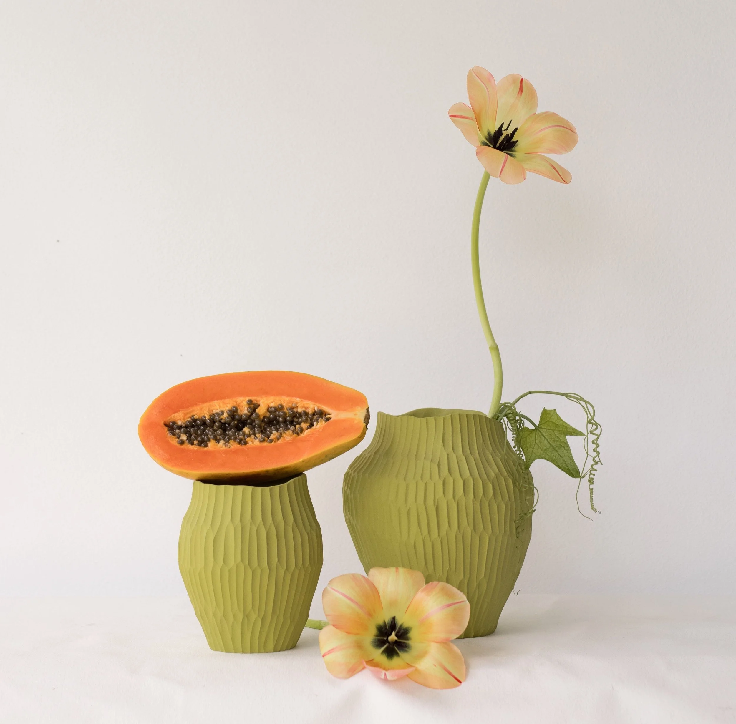 Arrangement of a papaya half and silk flowers in matching green vases on a white background.