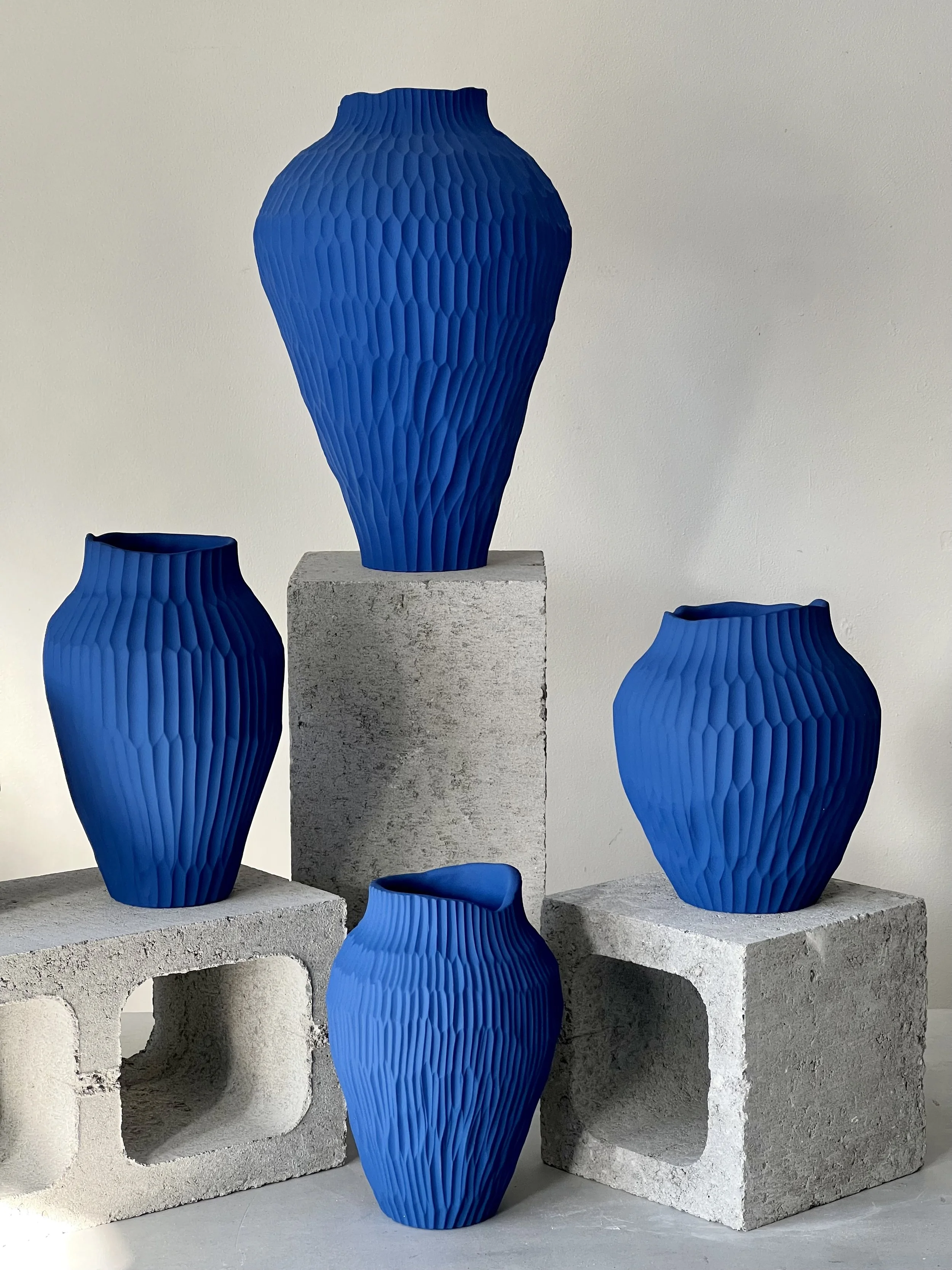Four textured blue vases arranged on concrete blocks against a neutral background.
