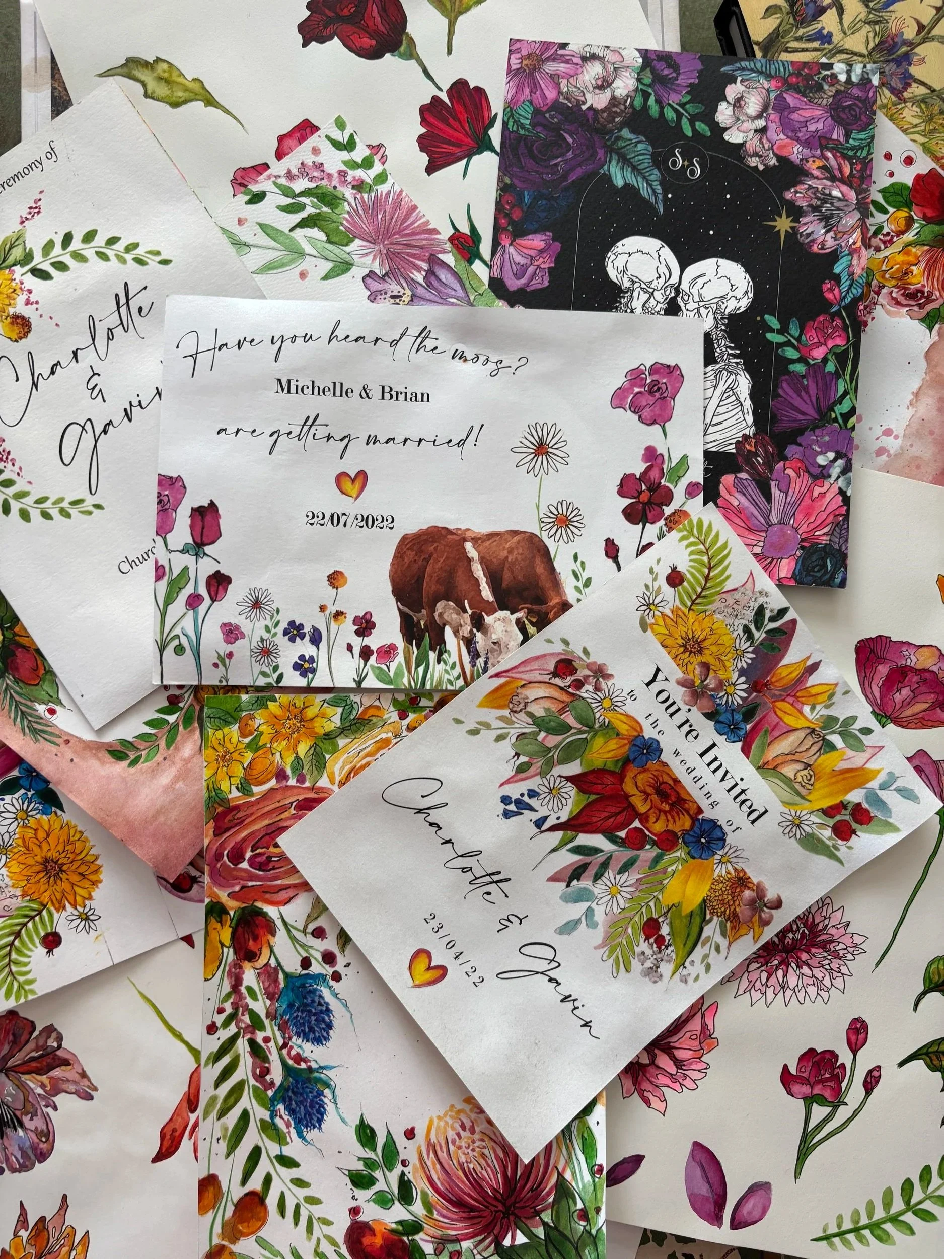 Collection of wedding invitation cards with floral designs and handwritten style text. One card has a black background with galaxy and moon illustrations, others feature colorful flowers and greenery.