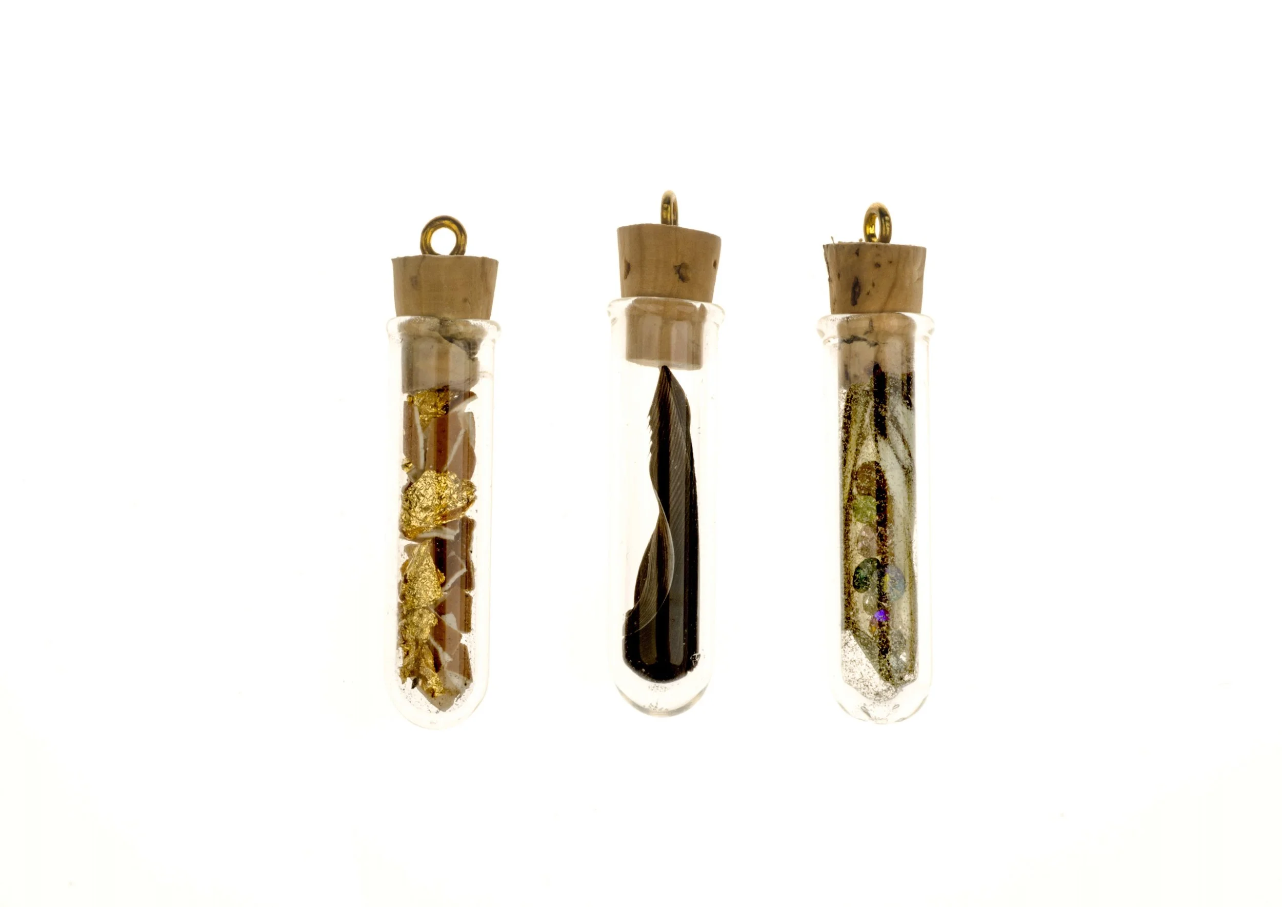 Three glass test tubes with cork stoppers, each containing different decorative objects, arranged in a row against a white background.