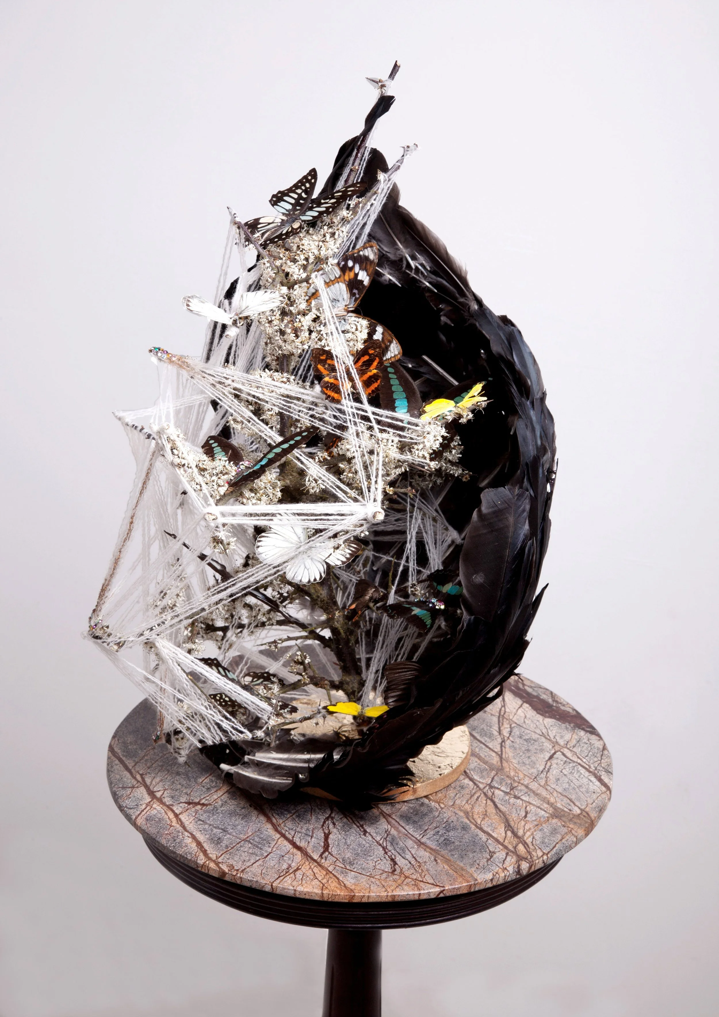 An art sculpture resembling a moon with embedded butterflies and spider webs, displayed on a round marble table.