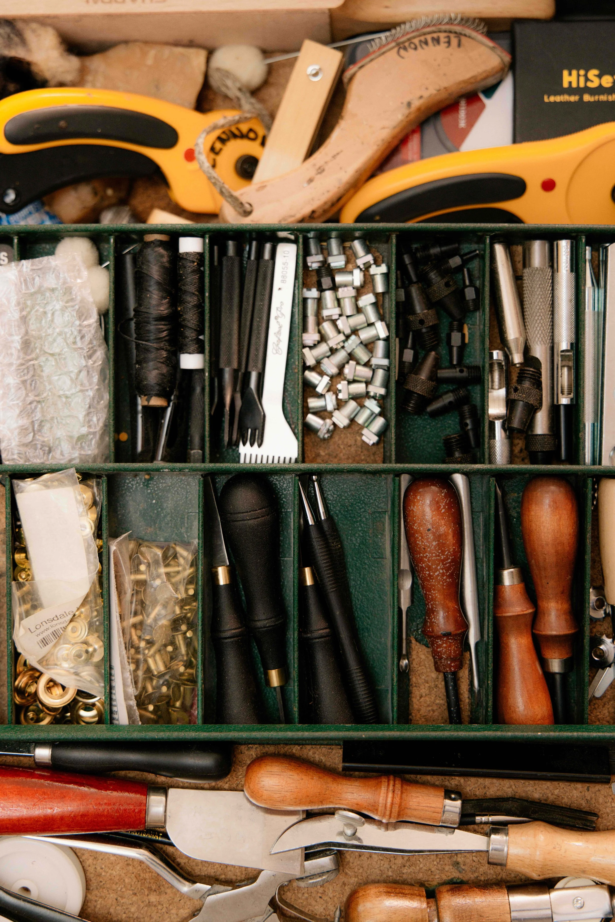 A collection of kitchen utensils including meat tenderizers, scissors, and various metal tools in a green storage tray with compartments.