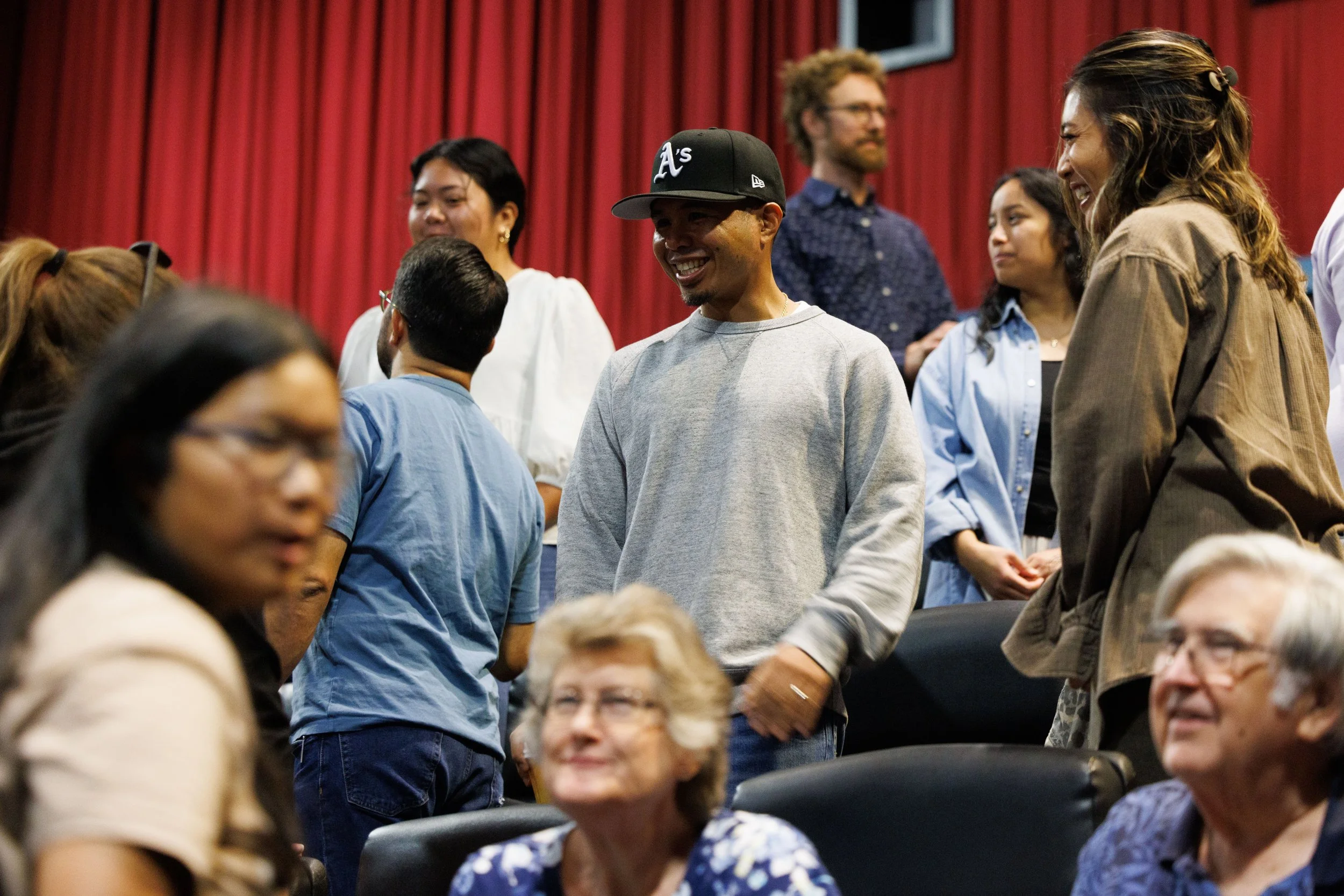 A group of diverse people engaging and smiling during an event with a red curtain backdrop