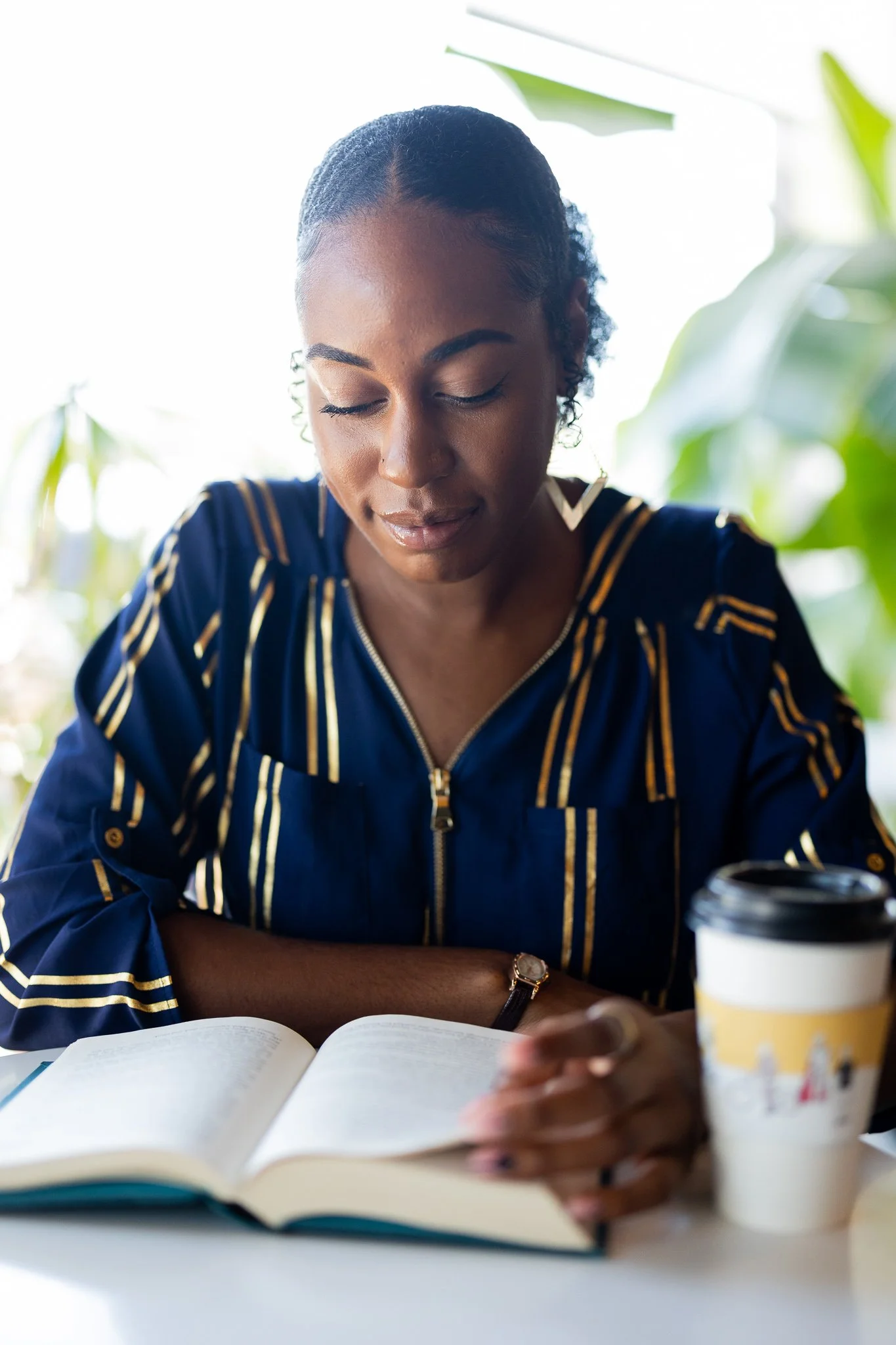 Woman reading a book at a table with a coffee cup.