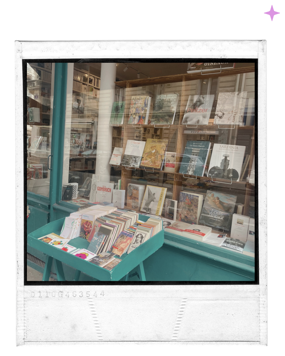 A bookstore window display with a teal cart filled with books and magazines outside, and shelves of books behind the glass window.