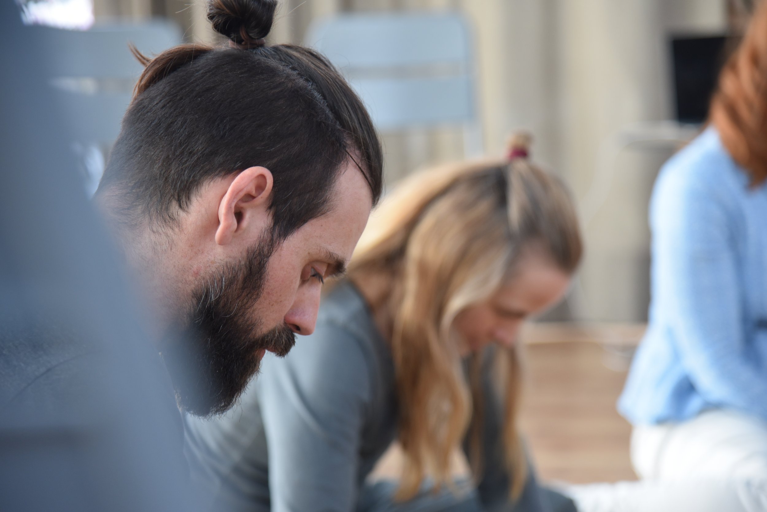 Mehrere Personen, die im Profil nach unten blicken, sitzen in einer Reihe in einem Raum.