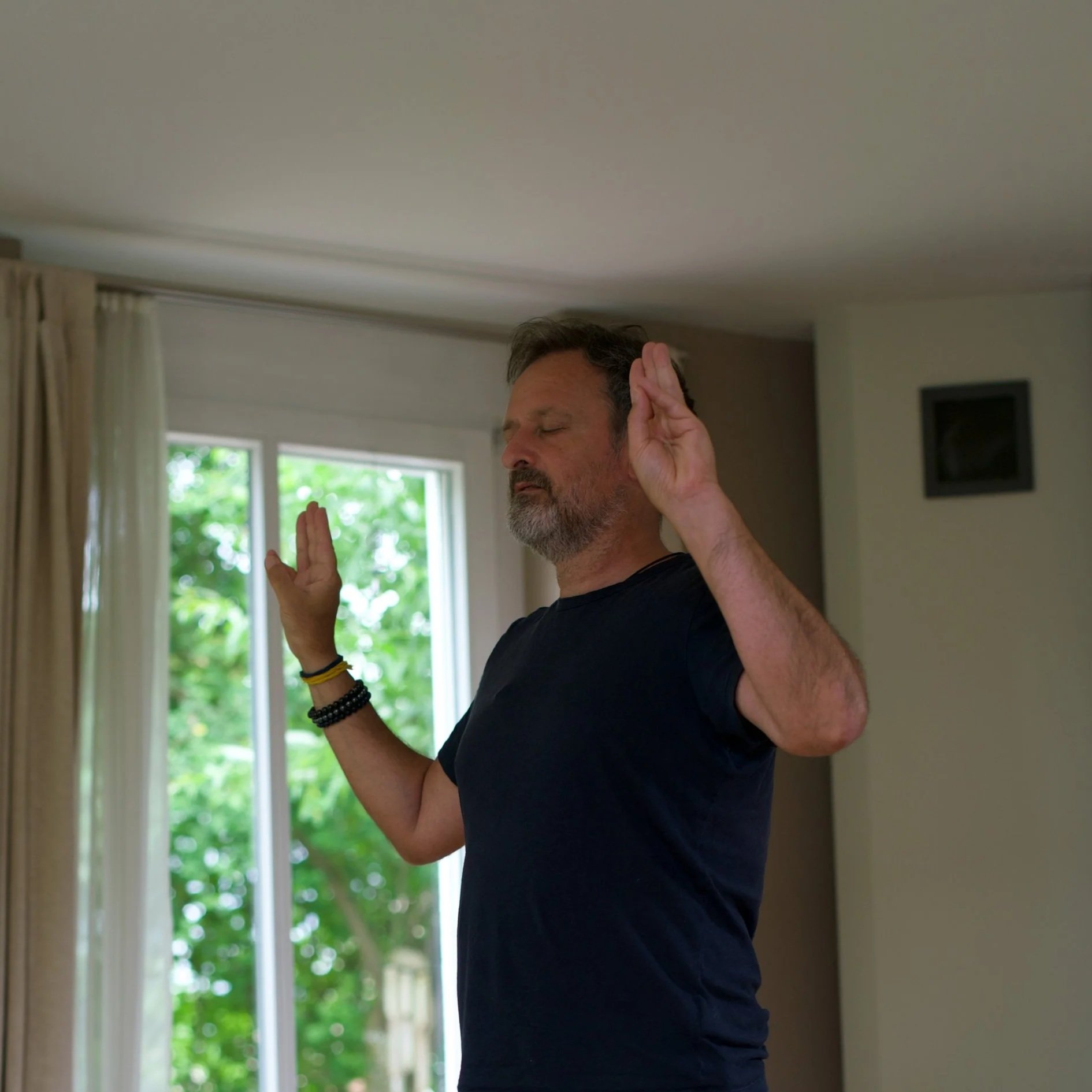 Ein Mann übt Meditation oder Achtsamkeit im Haus, mit geschlossenen Augen und erhobenen Händen.