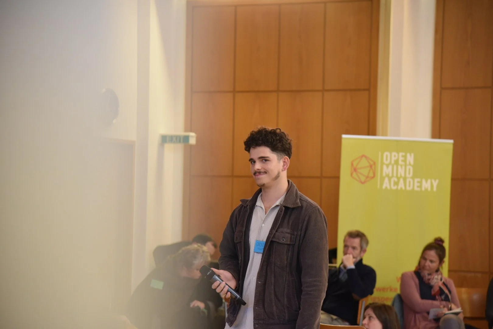 Junge Mann mit Mikrofonausweis bei Konferenz an der Open Mind Academy