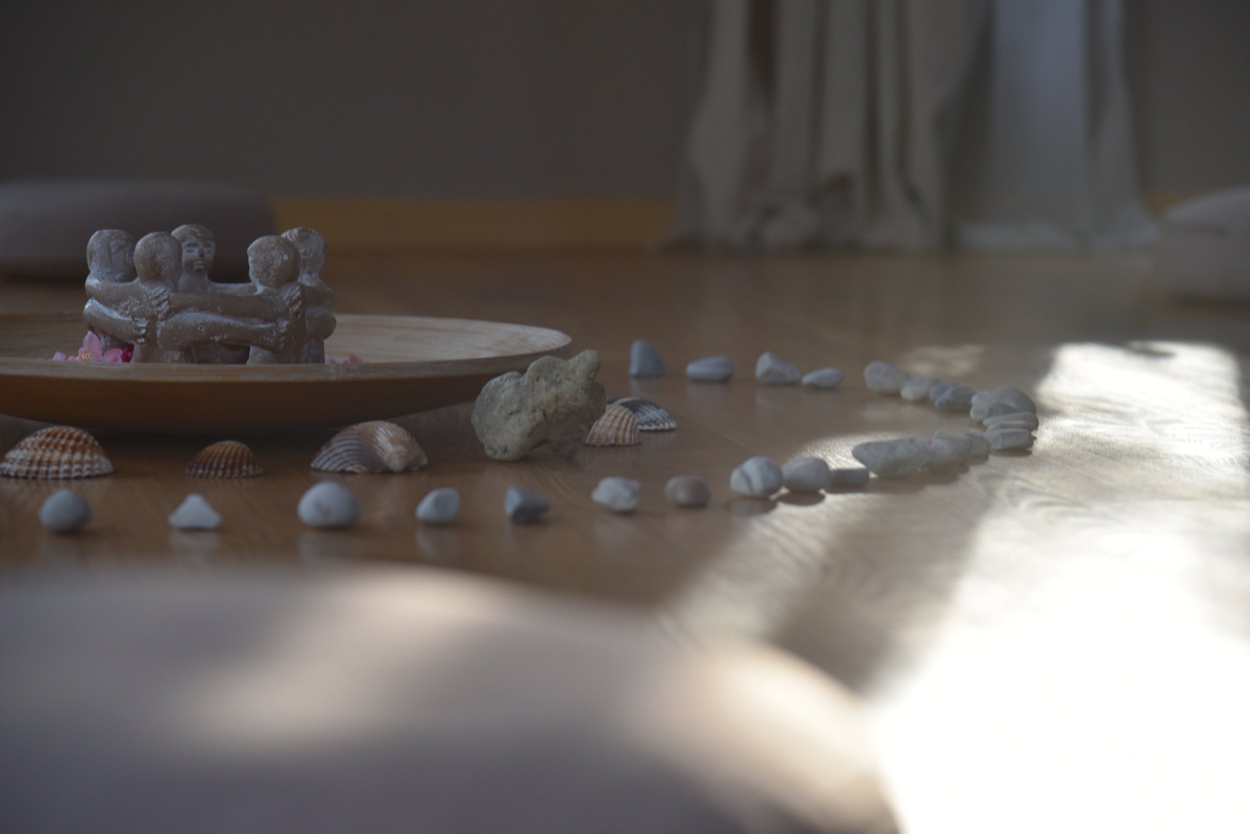 Sandfigurengruppe in Form eines Kreises, umgeben von Muscheln und Steinen auf einem Holztisch.