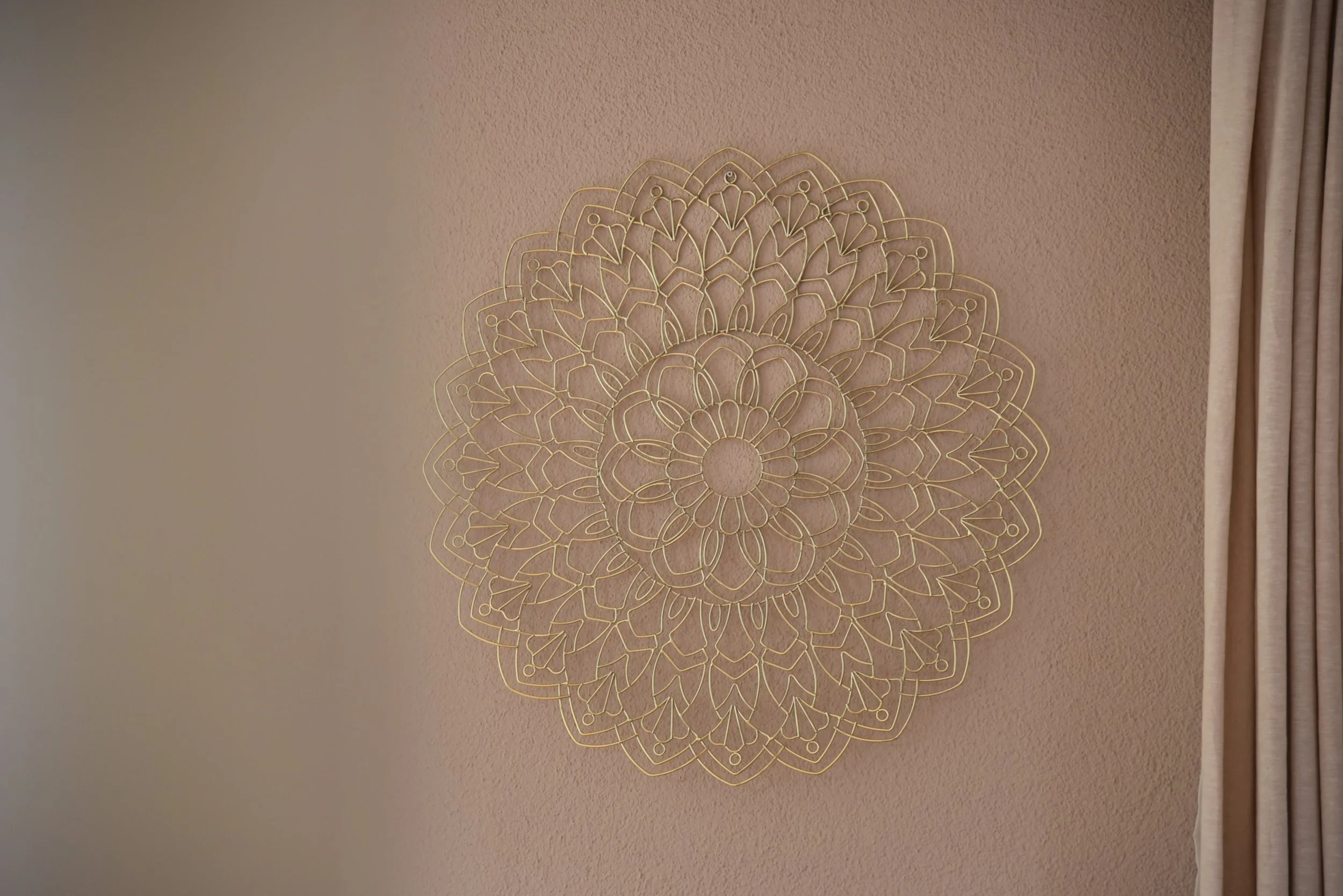 Goldene Wanddeko in Mandala-Form an einer pastellfarbenen Wand