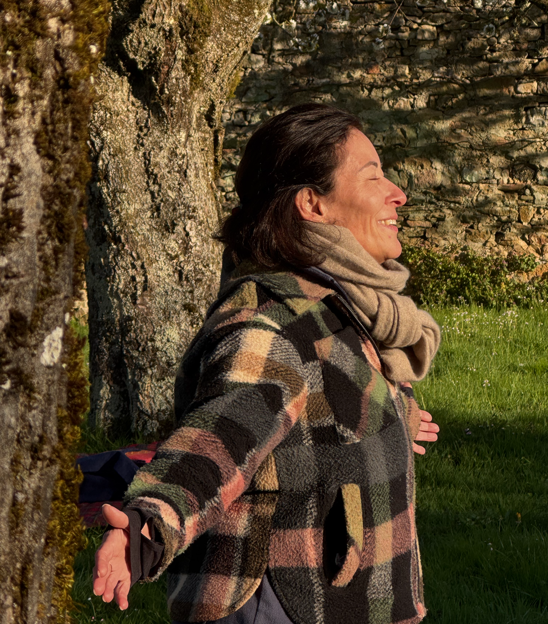 Frau lächelt entspannt an einem Baum im Freien bei Sonnenlicht.