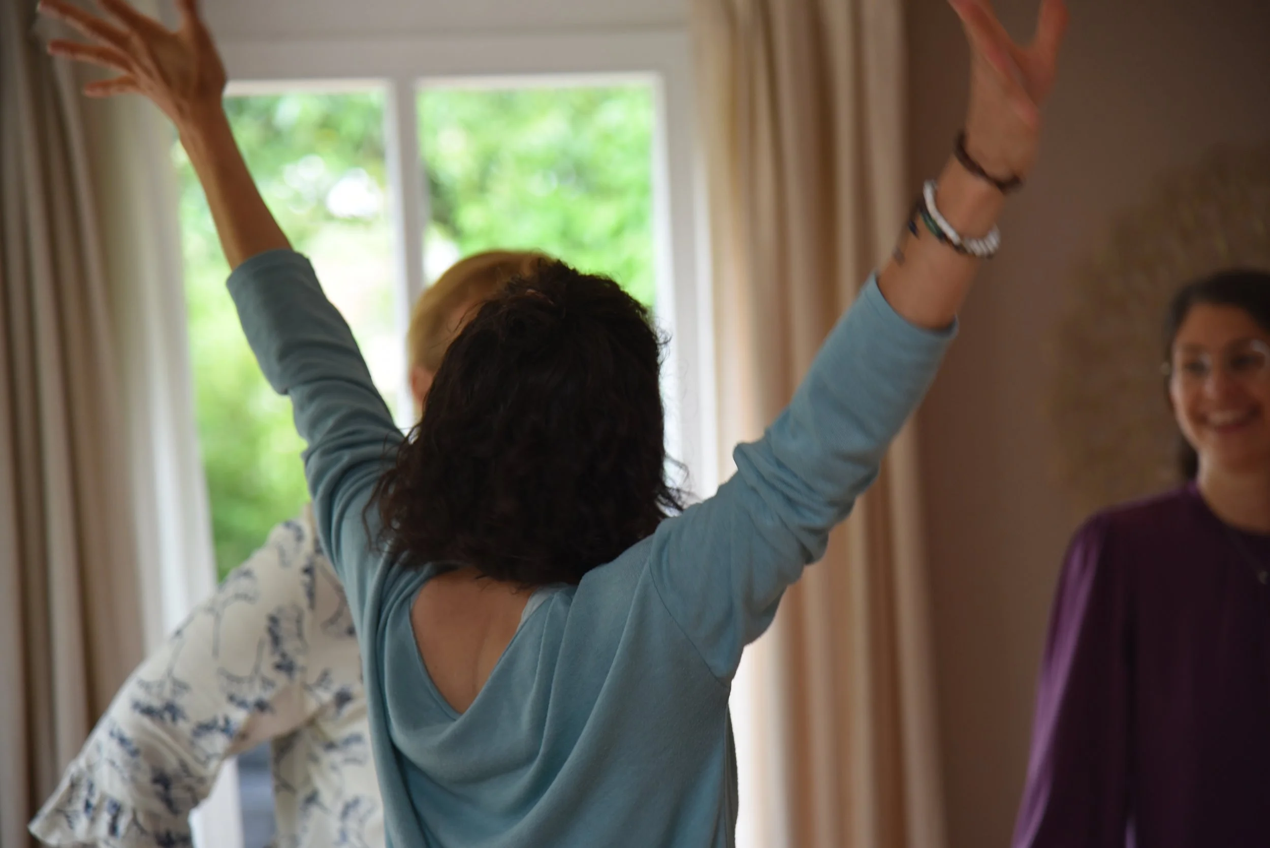 Drei Frauen lachen und freuen sich in einem Raum mit großen Fenstern und Vorhängen.