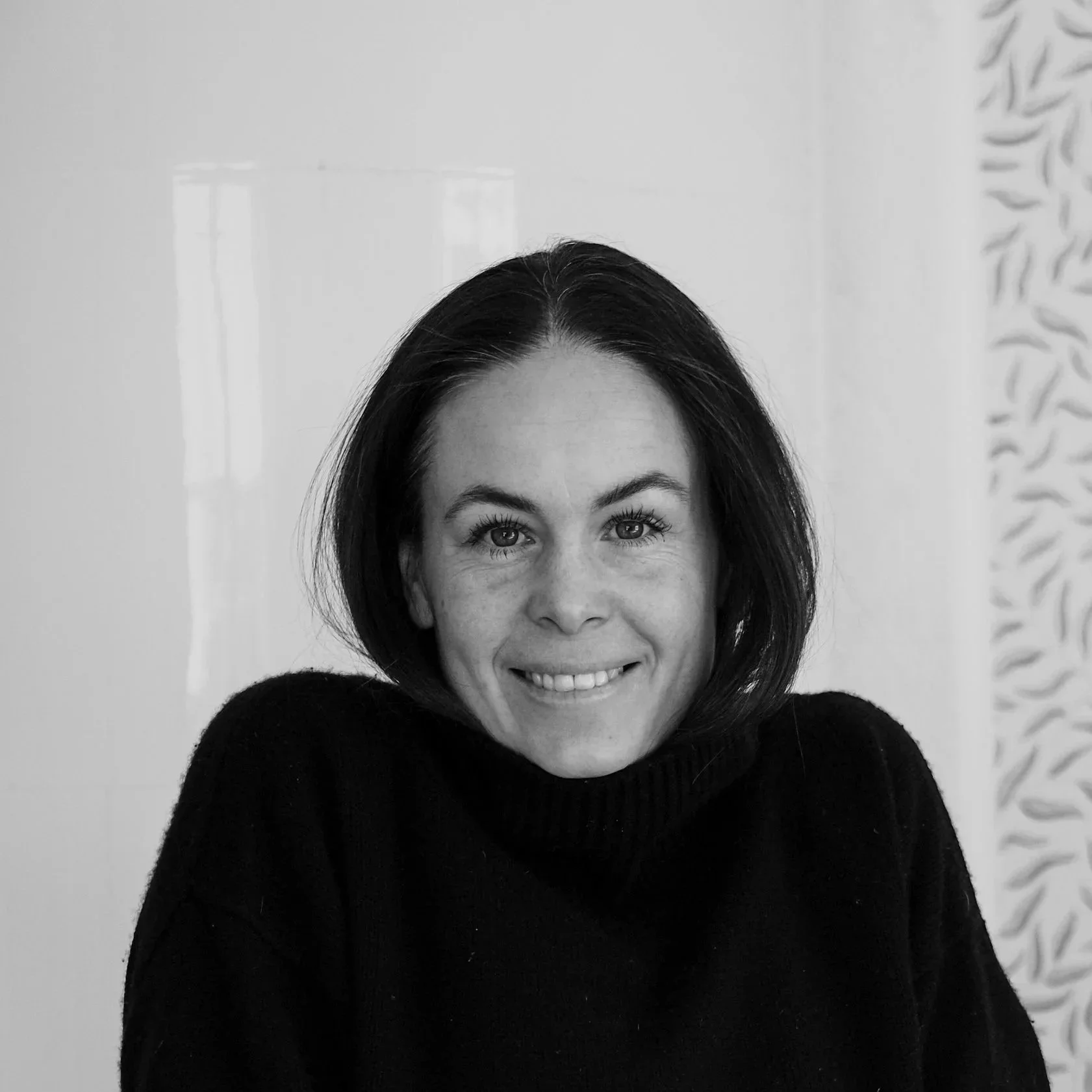 Svartvit porträtt av en leende kvinna med mörkt hår, bär en svart tröja.