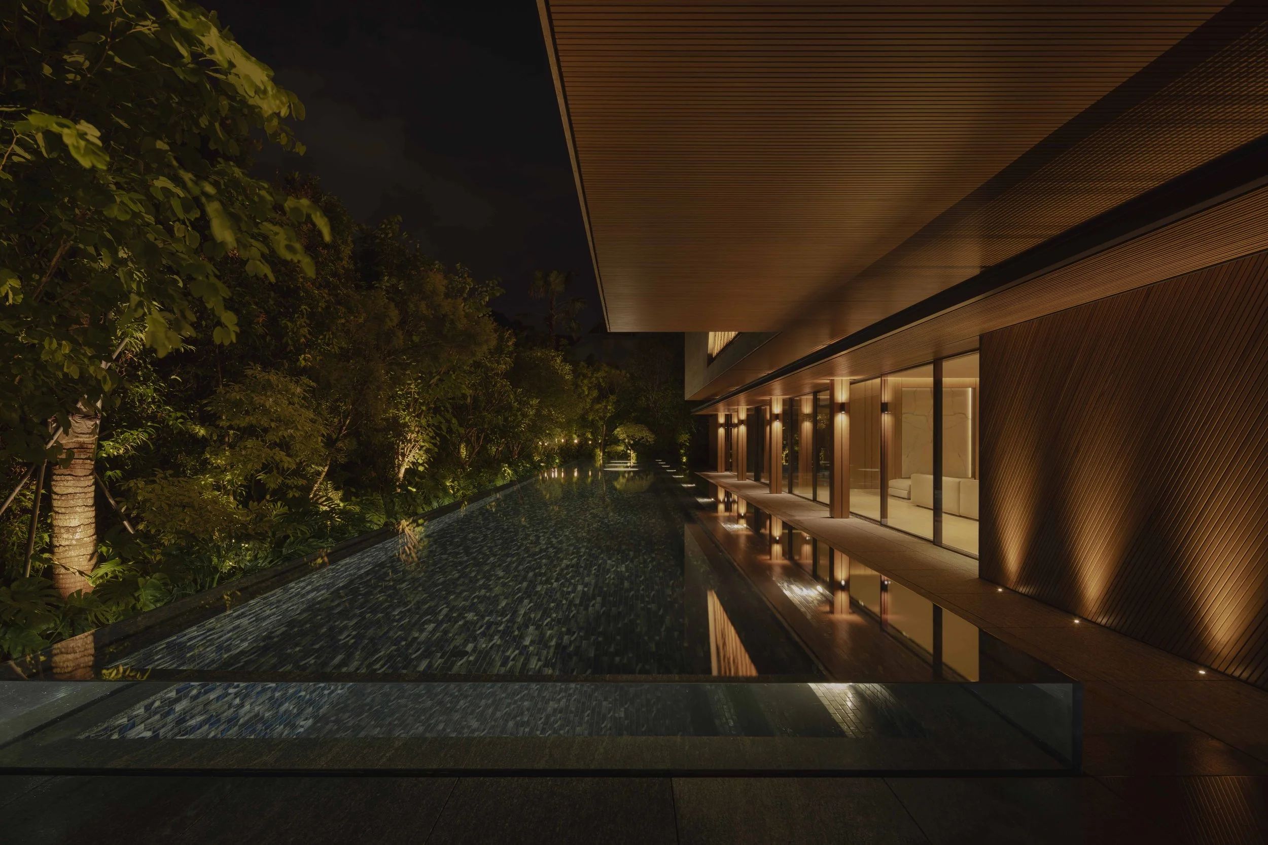 Night time view of a swimming pool by the side of a house