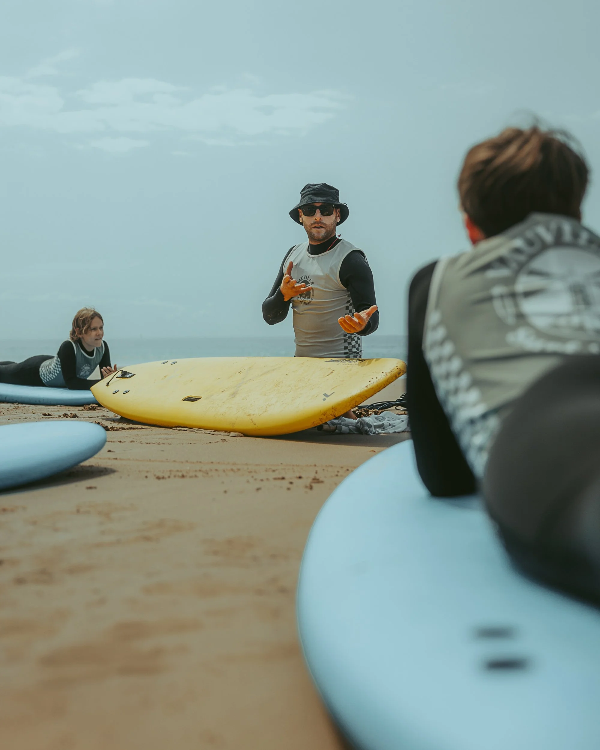 Trois personnes, dont deux hommes, près de planches de surf sur une plage.