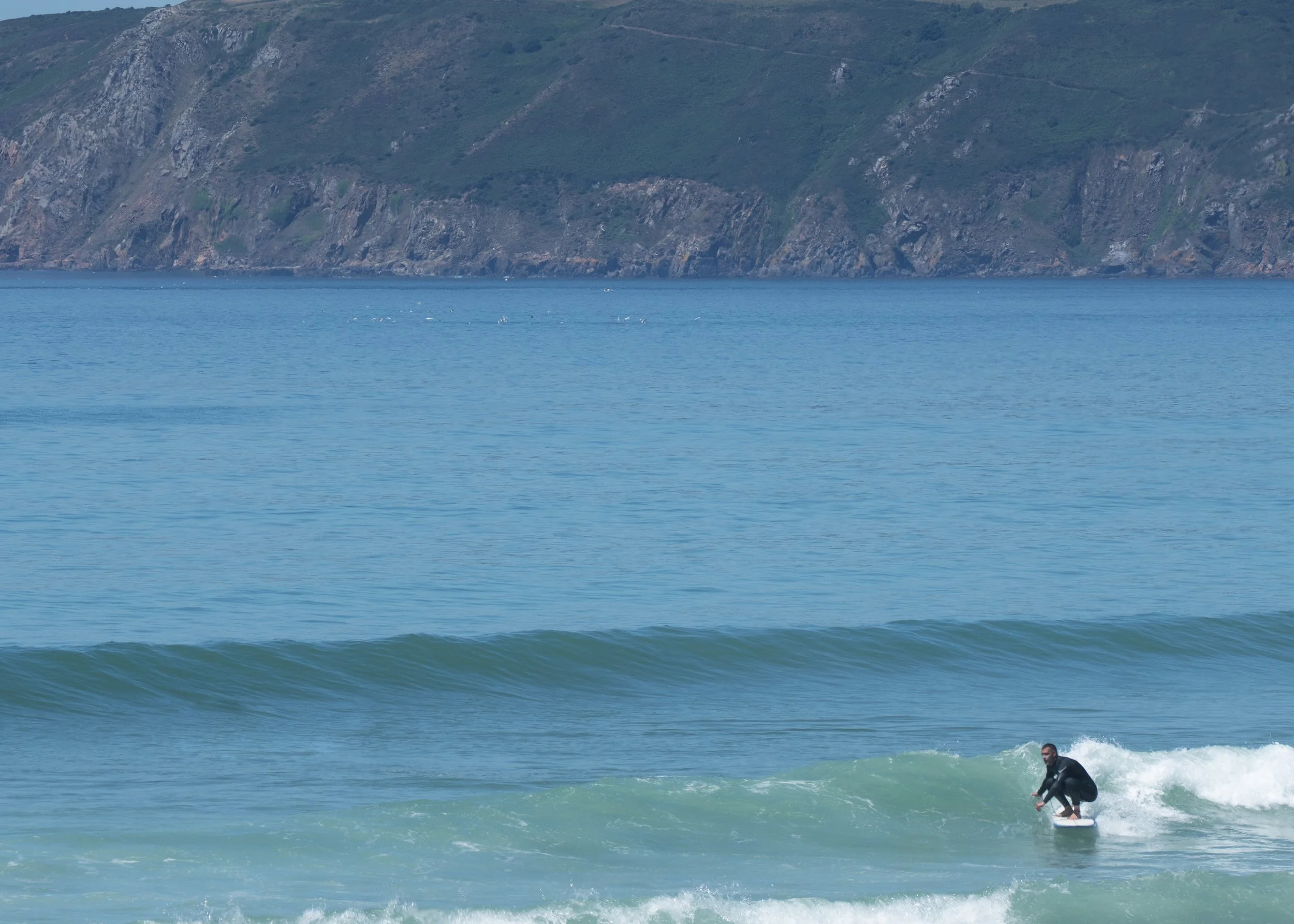 Un surfeur en train de faire du surf sur une vague à l'océan, avec une côte rocheuse en arrière-plan.