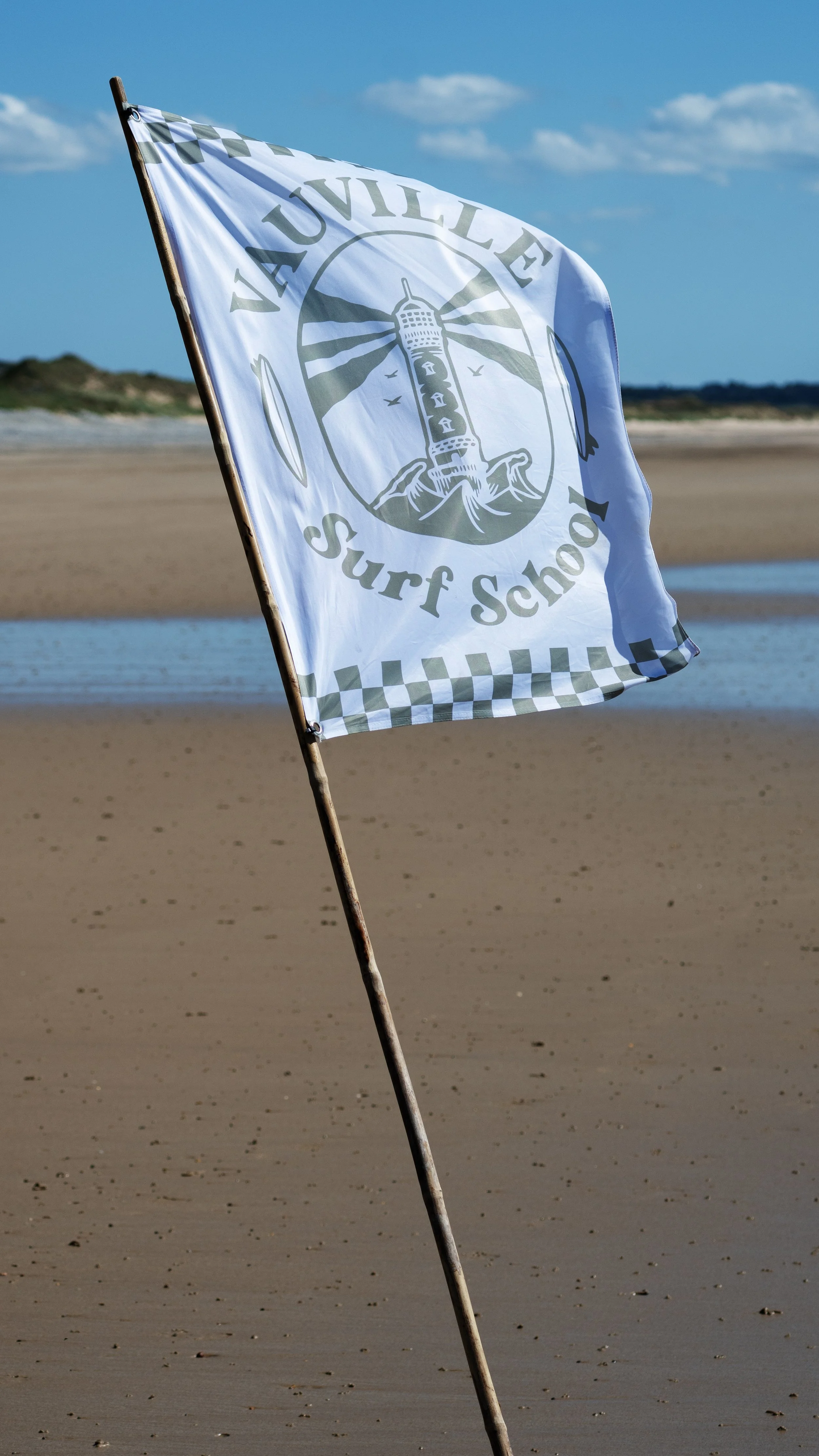 Drapeau de l'école de surf Vauville avec un phare, sur une plage