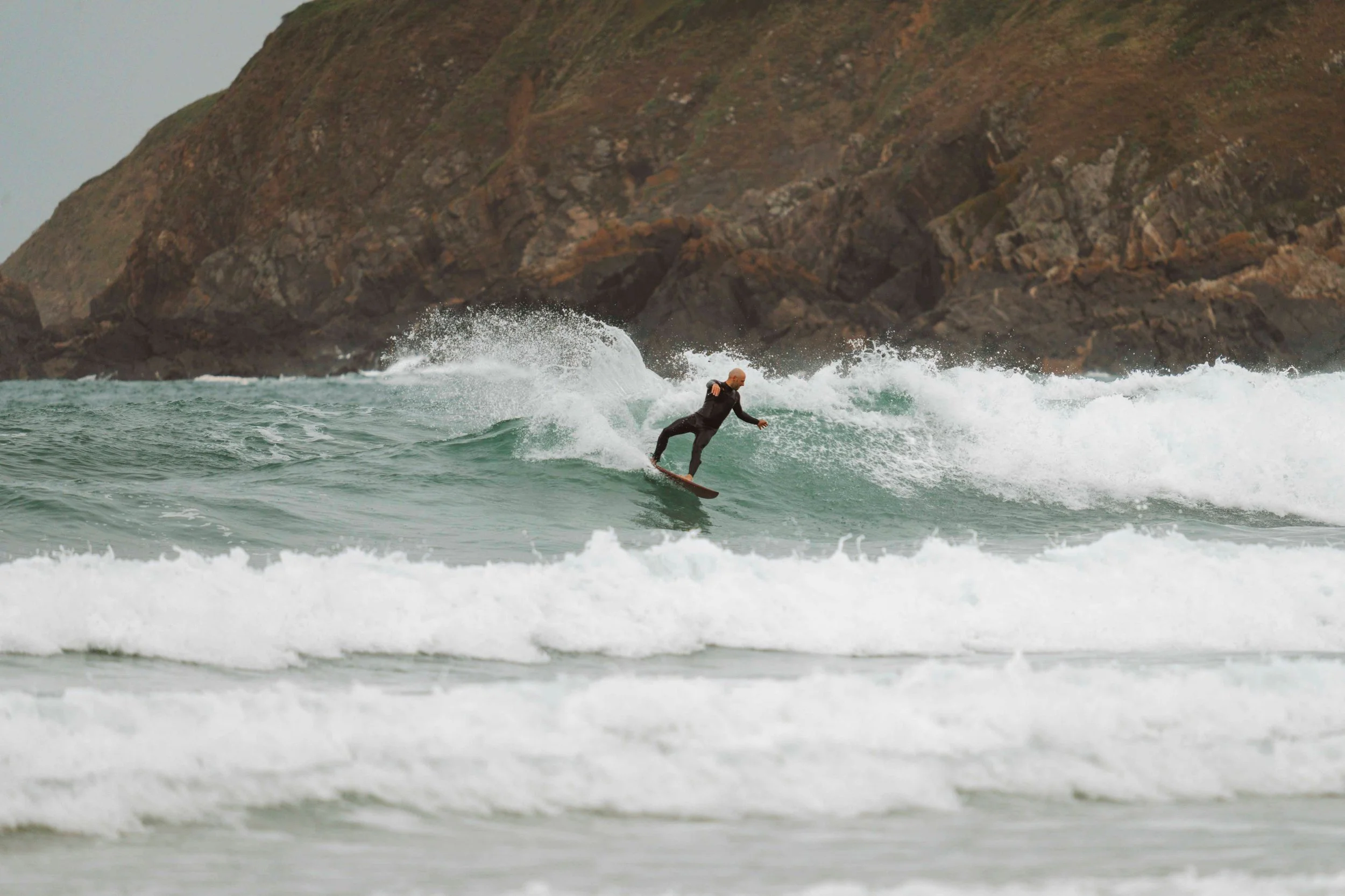 Surfeur en wetsuit noir riding une vague à proximité d'une falaise rocheuse.