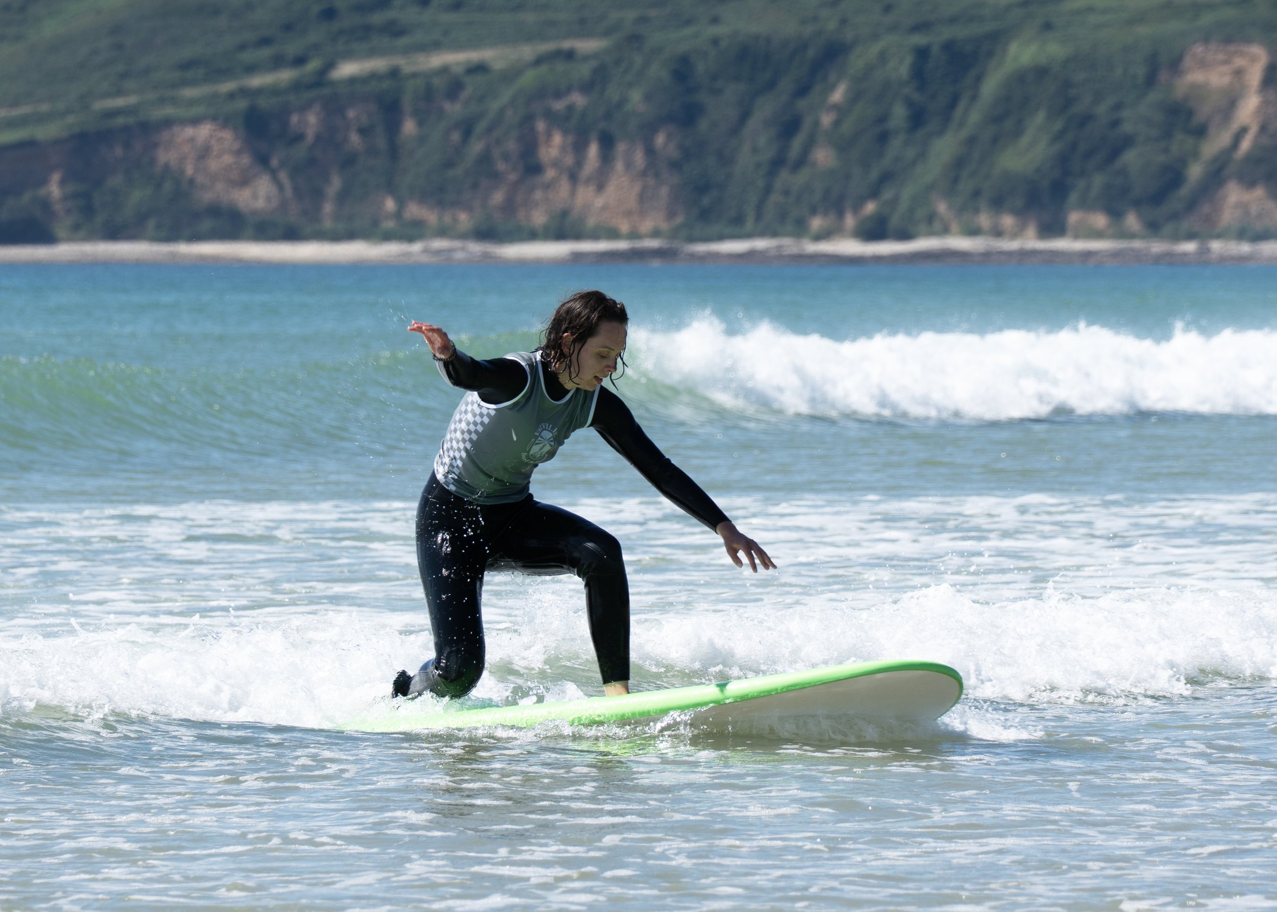 Femme débutante  sur une vague à la plage, portant une combinaison noire.