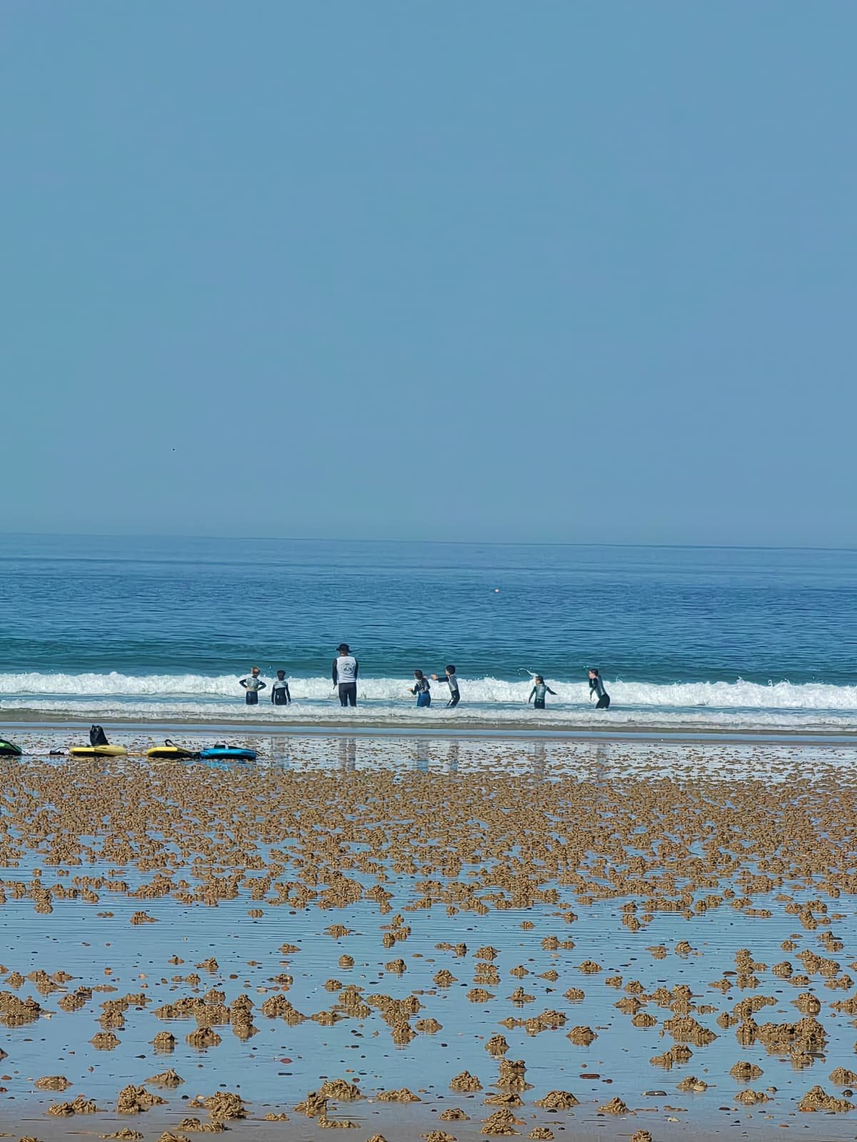 Groupe d'enfants et d'un adulte dans l'océan, plage de sable.