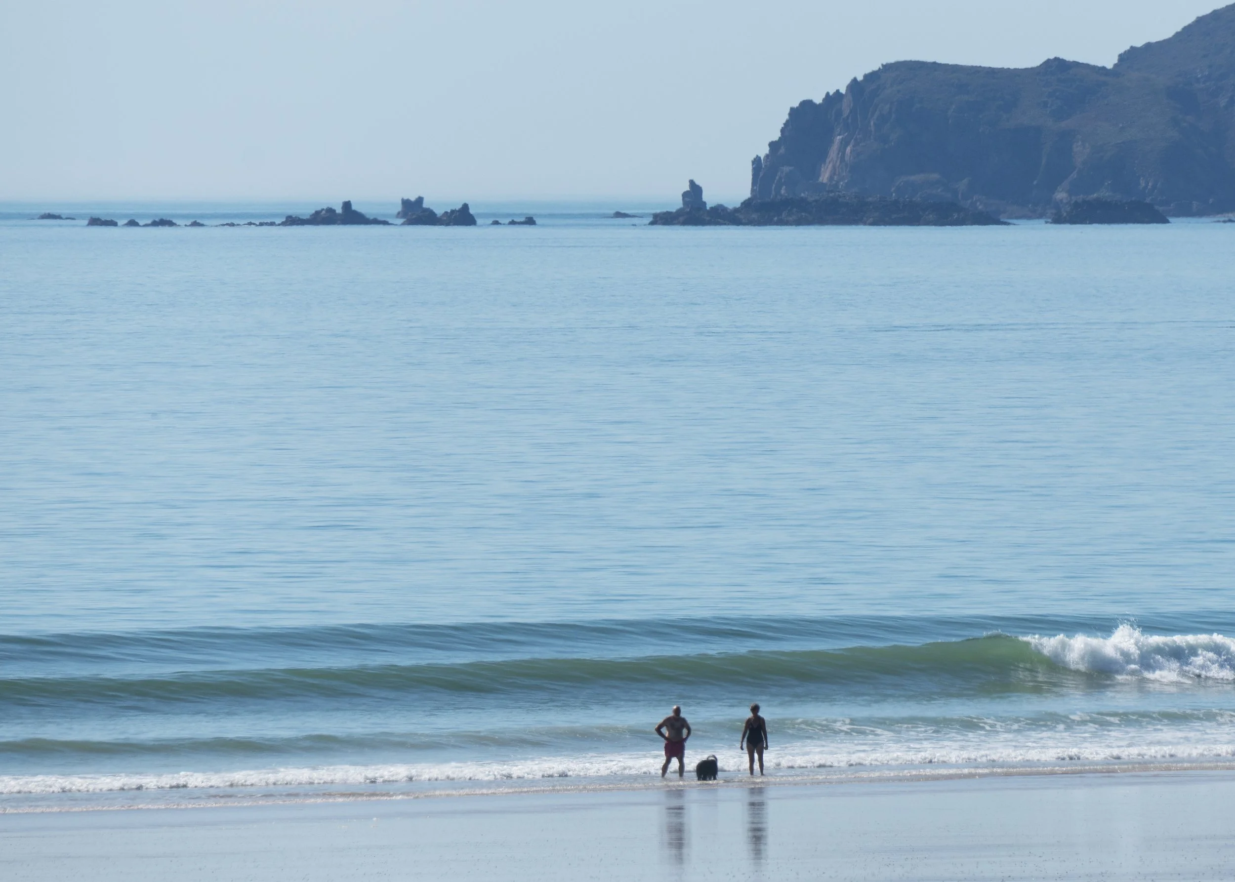 Plage avec deux personnes au bord de la mer, vagues et falaises à l'arrière-plan.